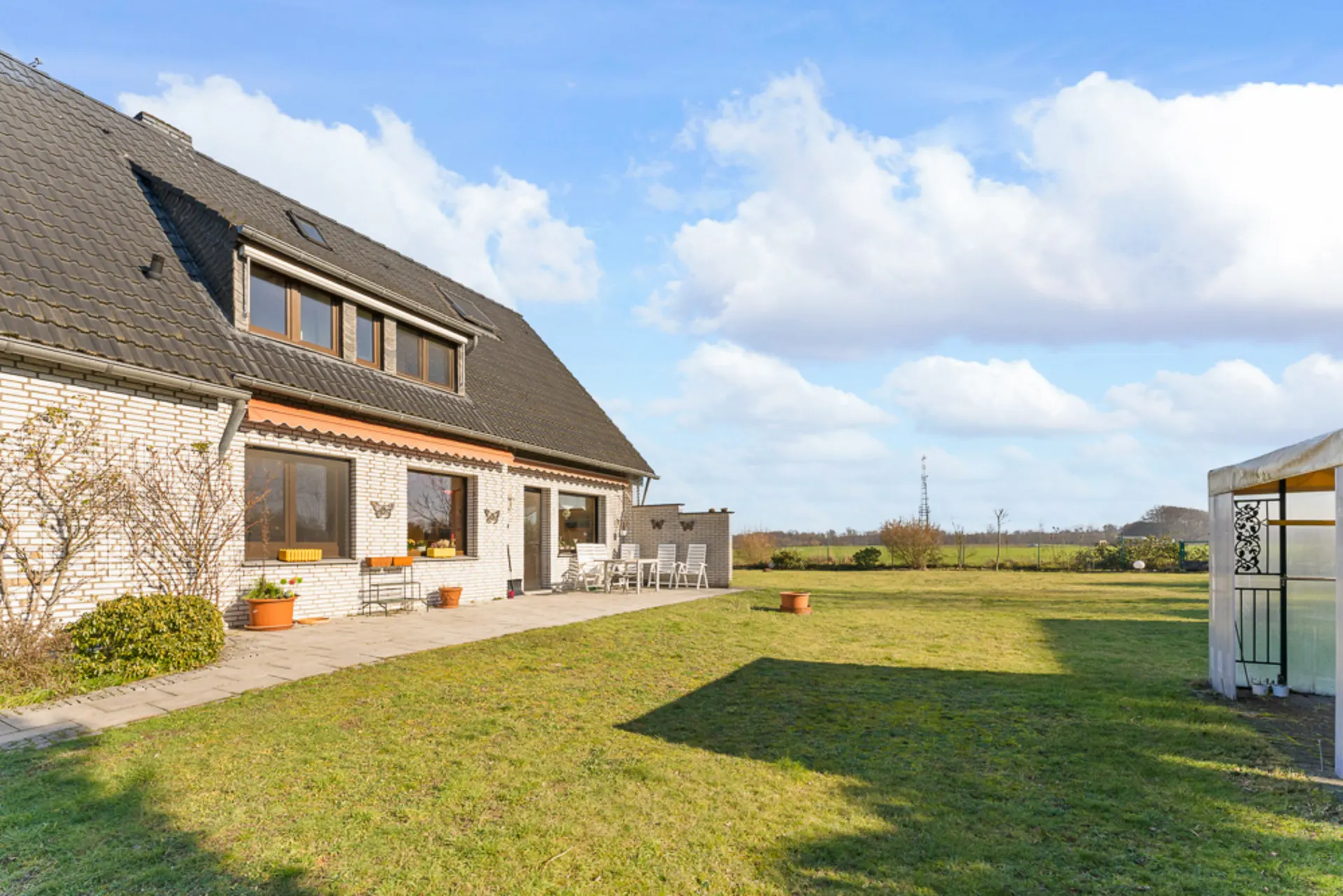 Großes Einfamilienhaus mit Terrasse und weitem Garten an einem sonnigen Tag.