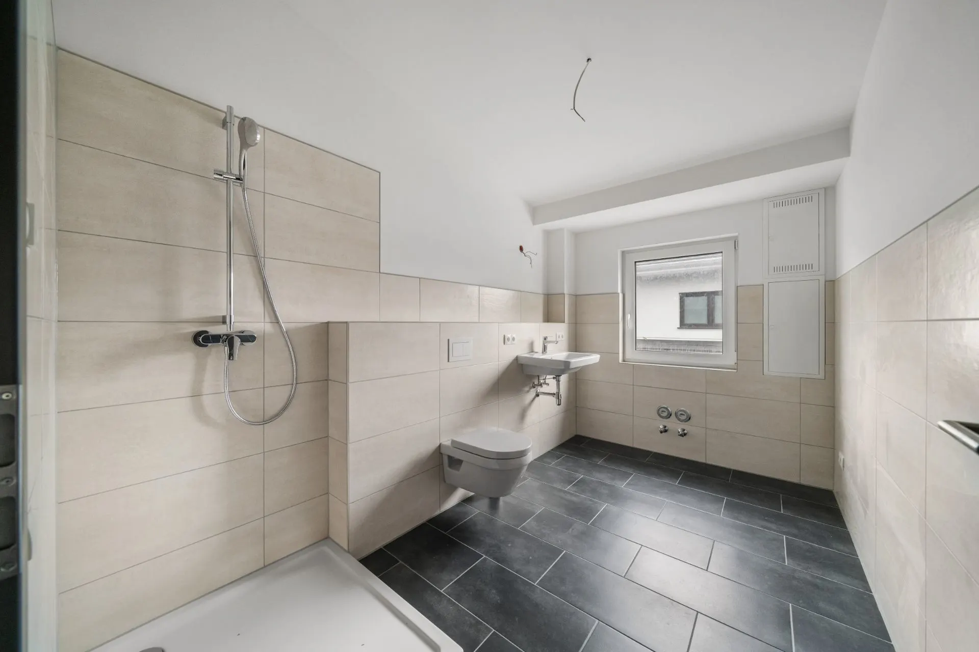 Modernes, leeres Badezimmer mit Dusche, Wand-WC, Waschbecken und Fenster.