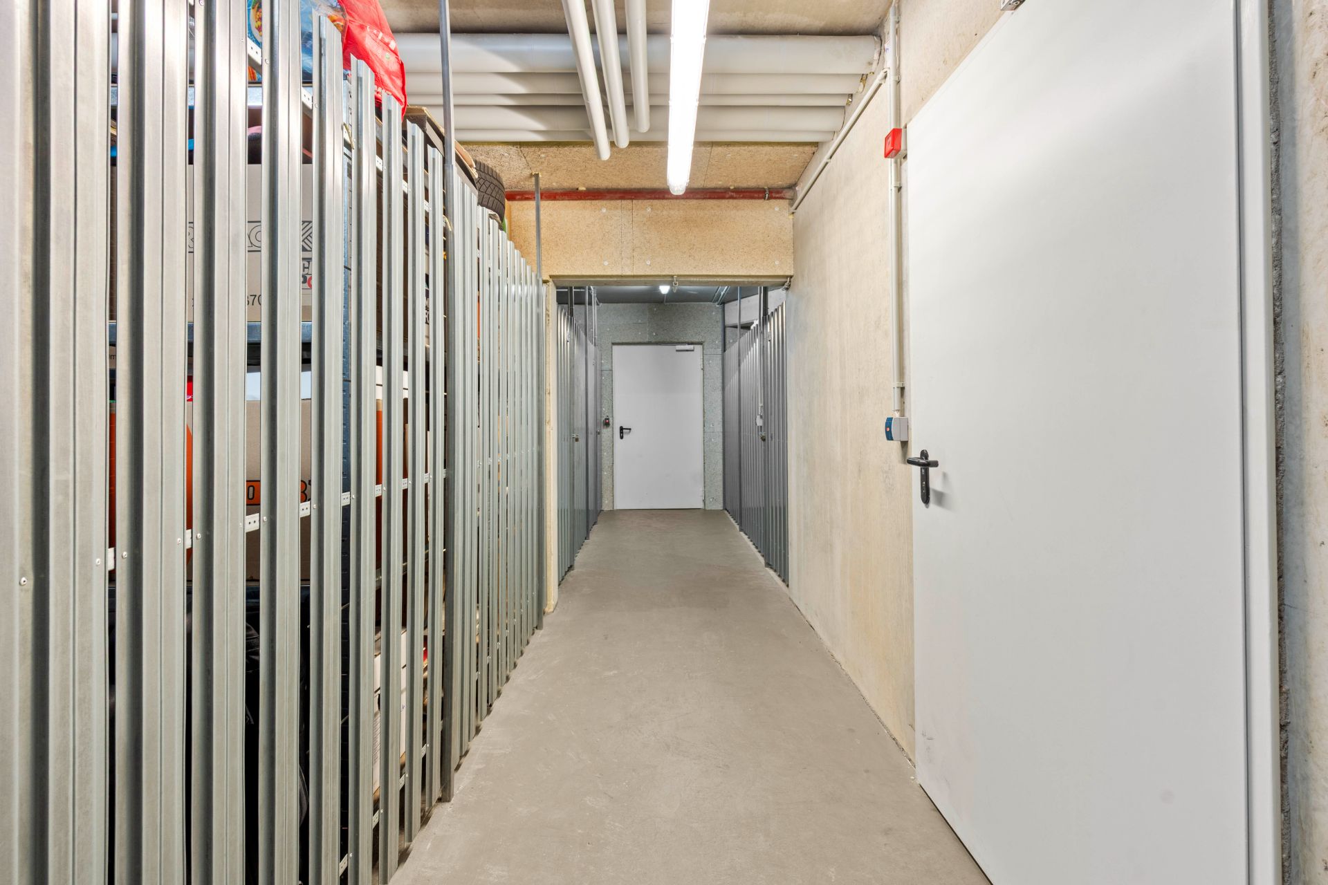 Heller Flur mit Metallgitter-Abteilen und Türen in einem Kellerraum.