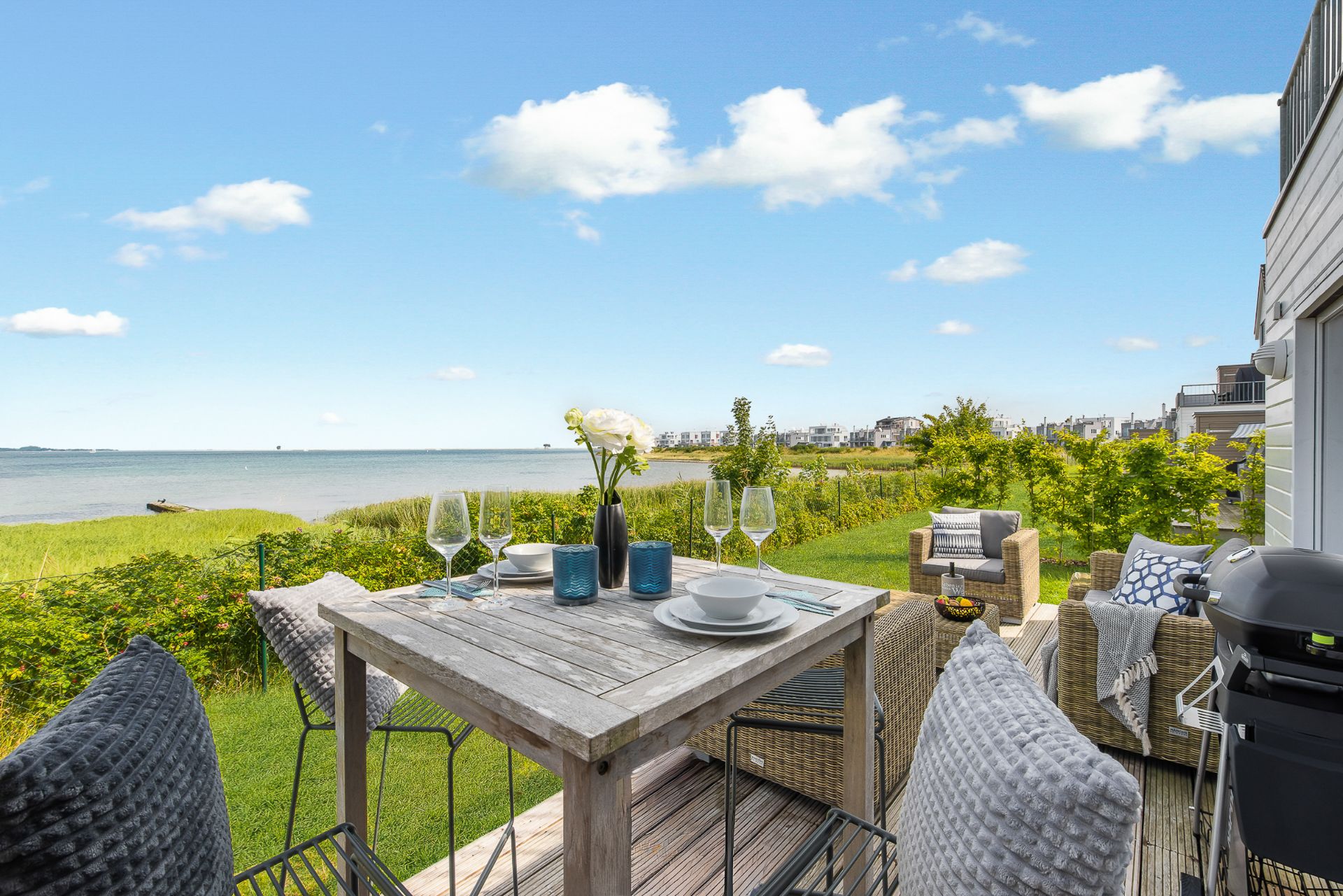 Terrasse mit Holztisch, vier Stühlen, Sofa und Blick auf das Meer und Garten.