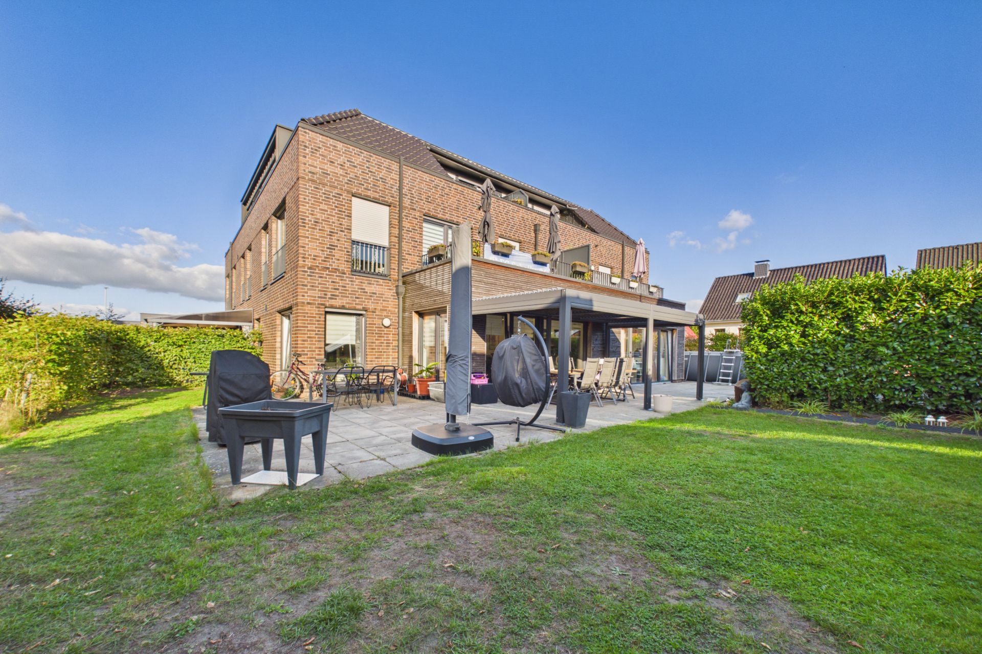 Backstein-Wohnhaus mit Terrasse, Gartenmöbeln und großem Rasen im Garten.