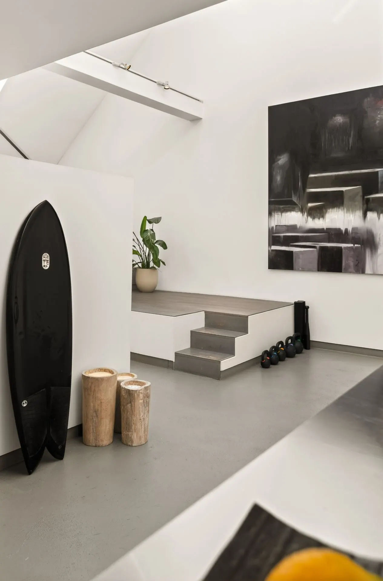 Modernes Wohnzimmer mit Surfbrett, Hockern, Pflanze, Stufen und abstraktem Gemälde an der Wand.