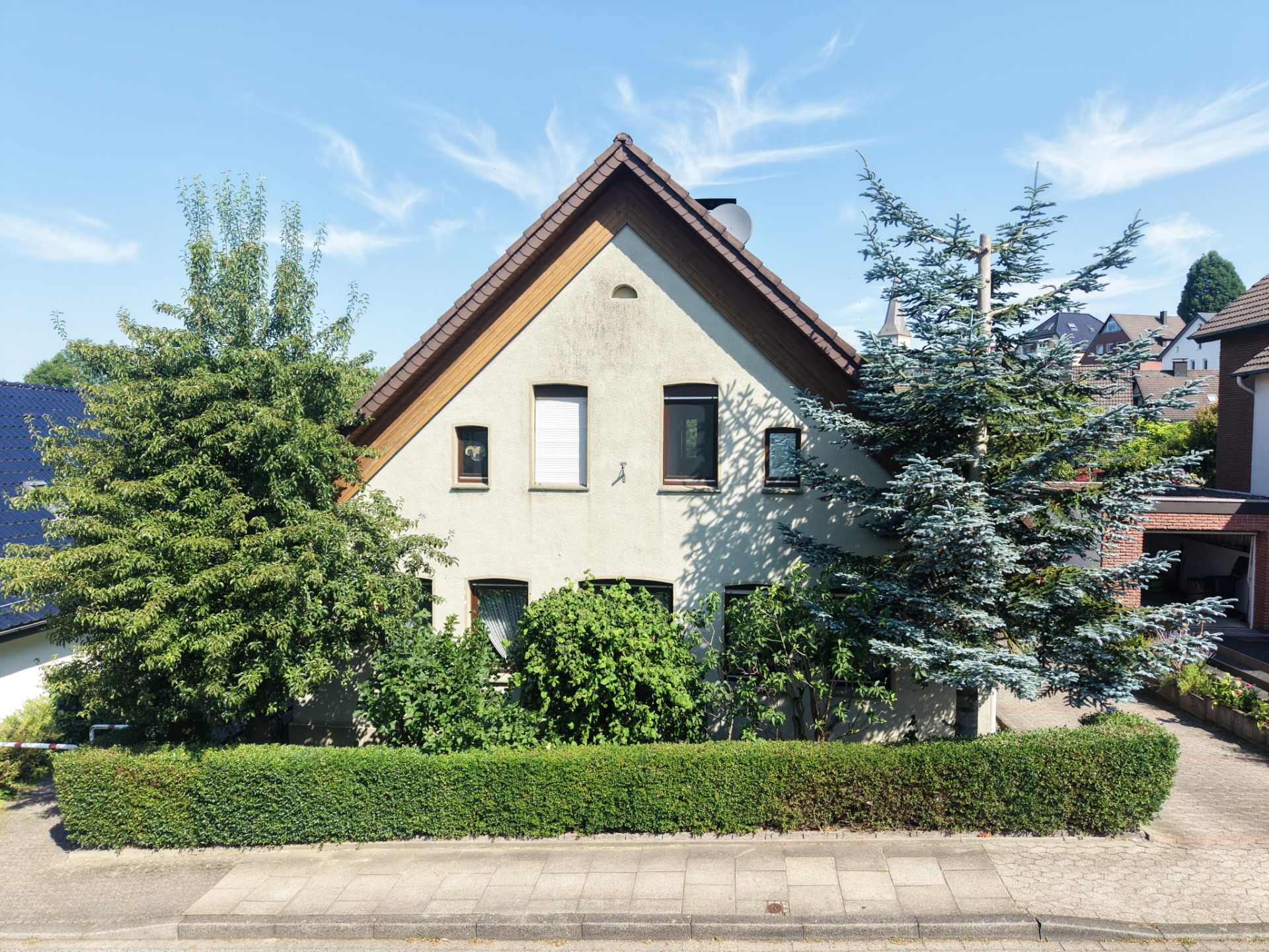 Ein Einfamilienhaus mit Satteldach, umgeben von Bäumen und einer Hecke an der Vorderseite.