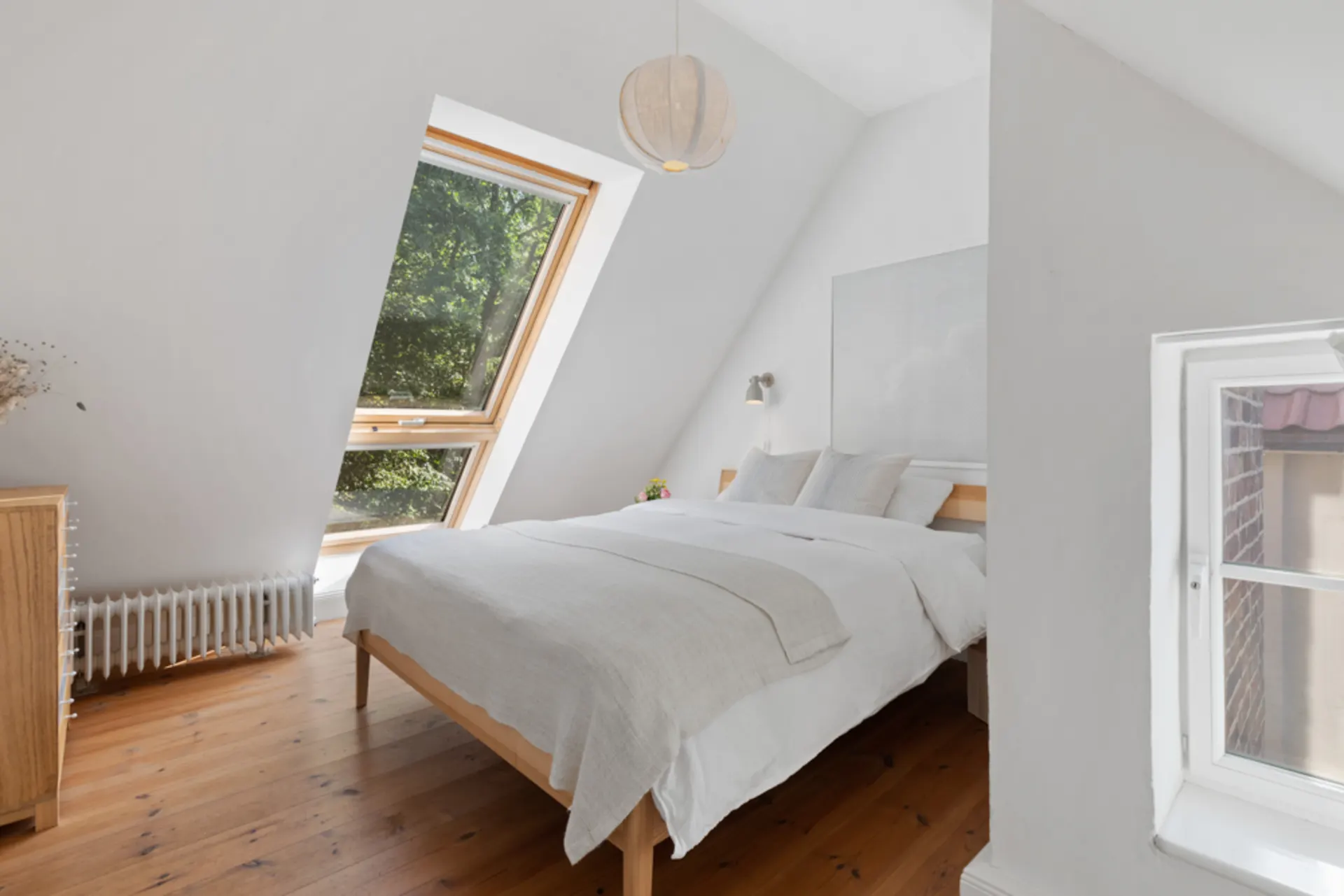 Helles Schlafzimmer mit großem Dachfenster, Holzboden und Doppelbett.