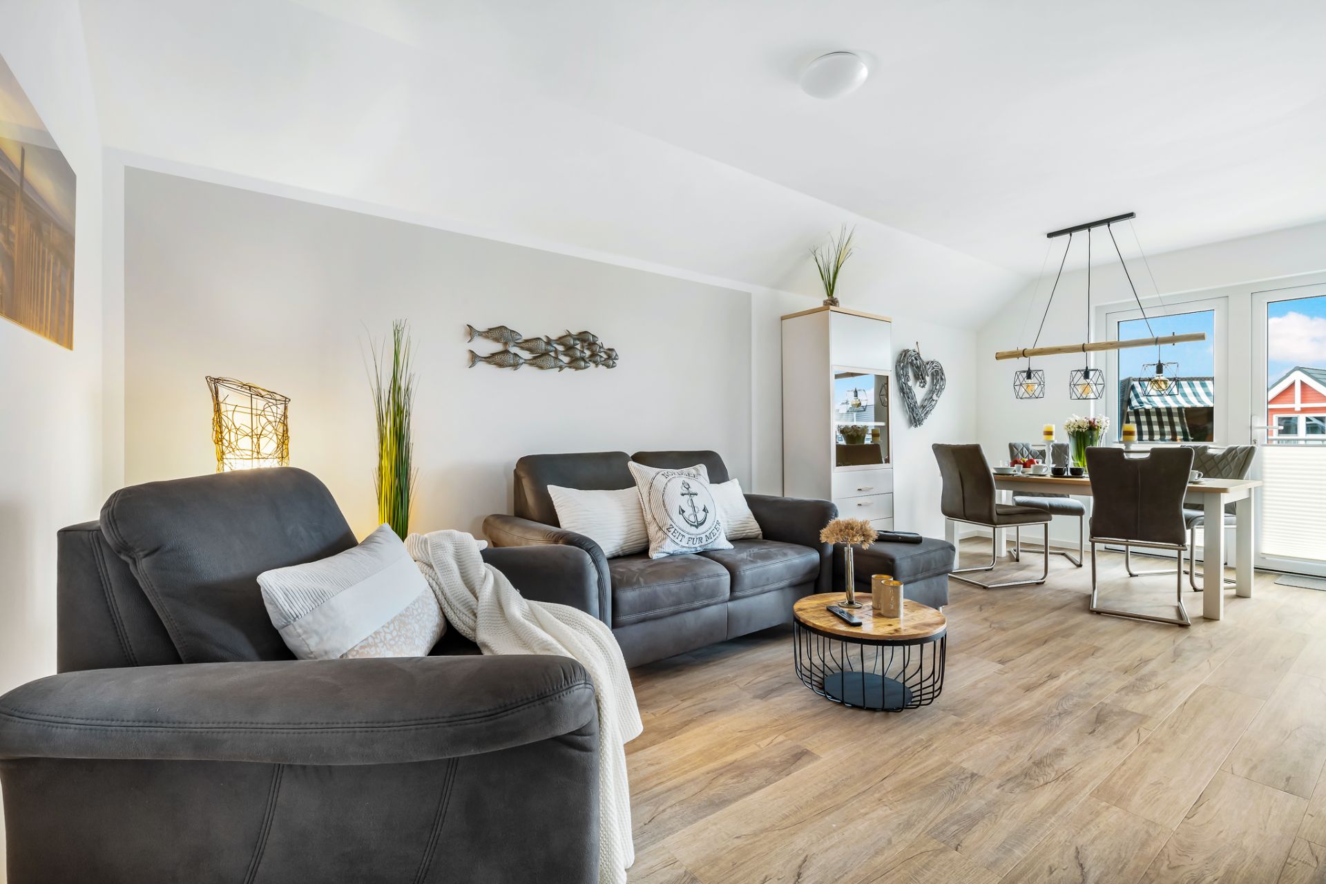 Helles Wohnzimmer mit Sofa, Sessel, Esstisch und großen Fenstern, Holzboden.