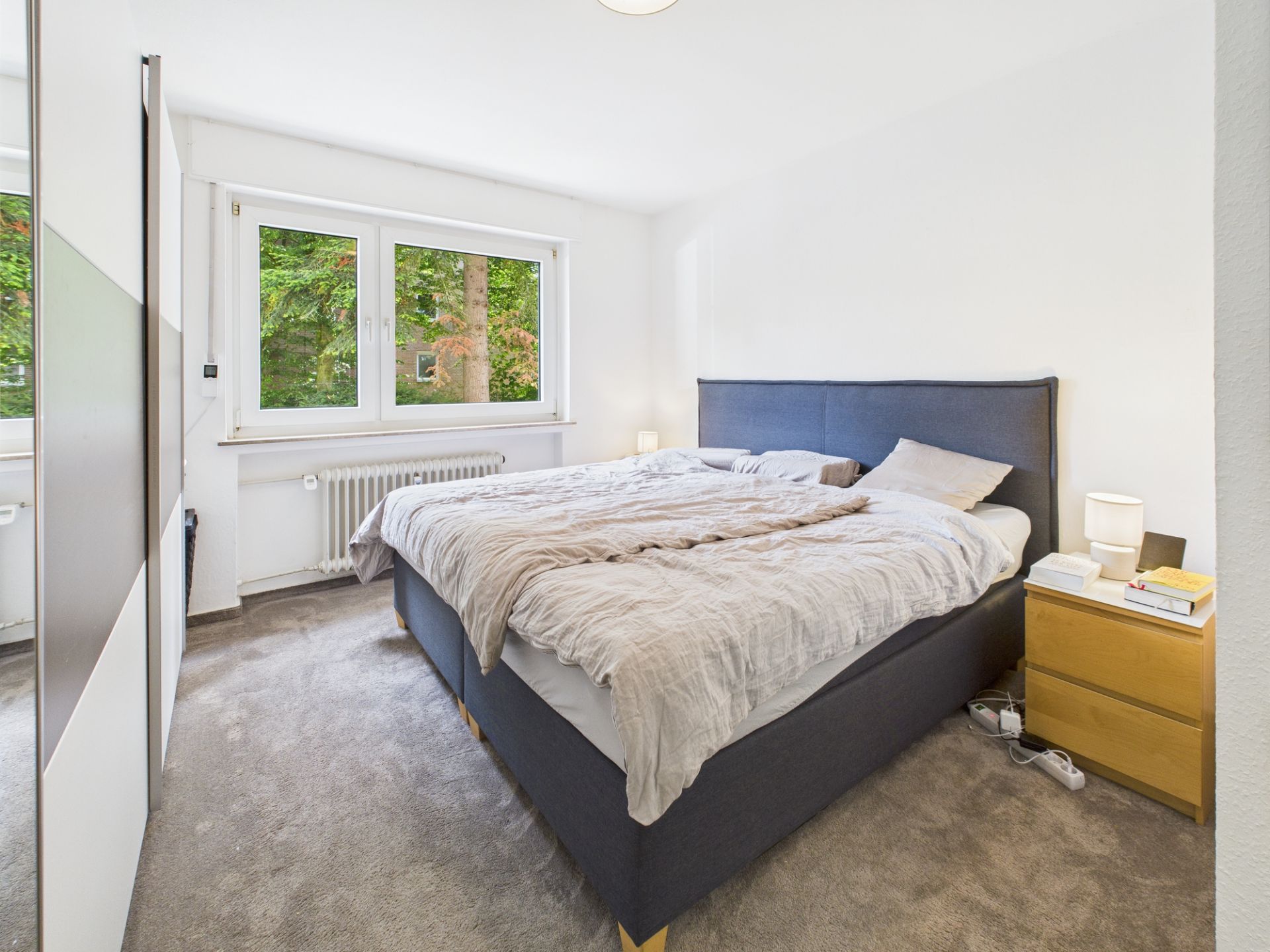 Helles Schlafzimmer mit Doppelbett, Nachttisch und großem Fenster mit Blick ins Grüne.