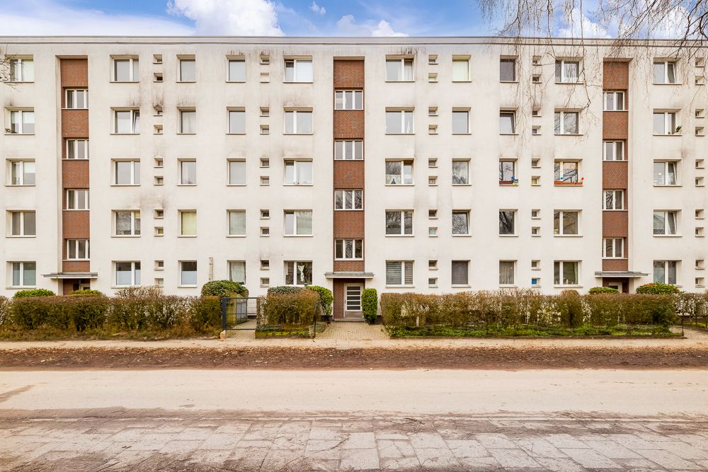 Mehrstöckiges Wohnhaus mit vielen Fenstern und kleinen Vorgärten, Blick auf die Hausfront.