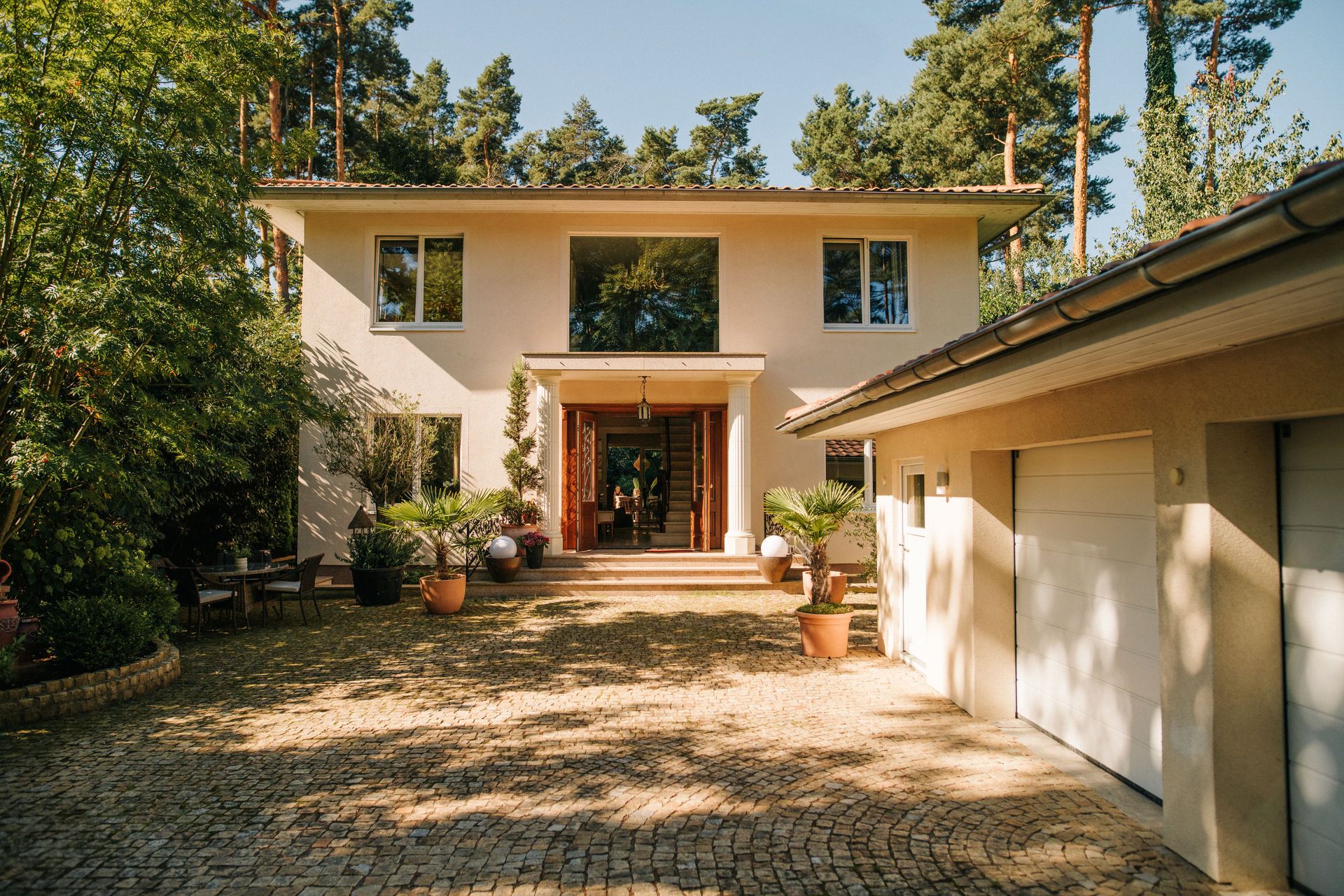 Einfamilienhaus mit zwei Etagen, großem Eingang und Garage, umgeben von Bäumen und Pflanzen.