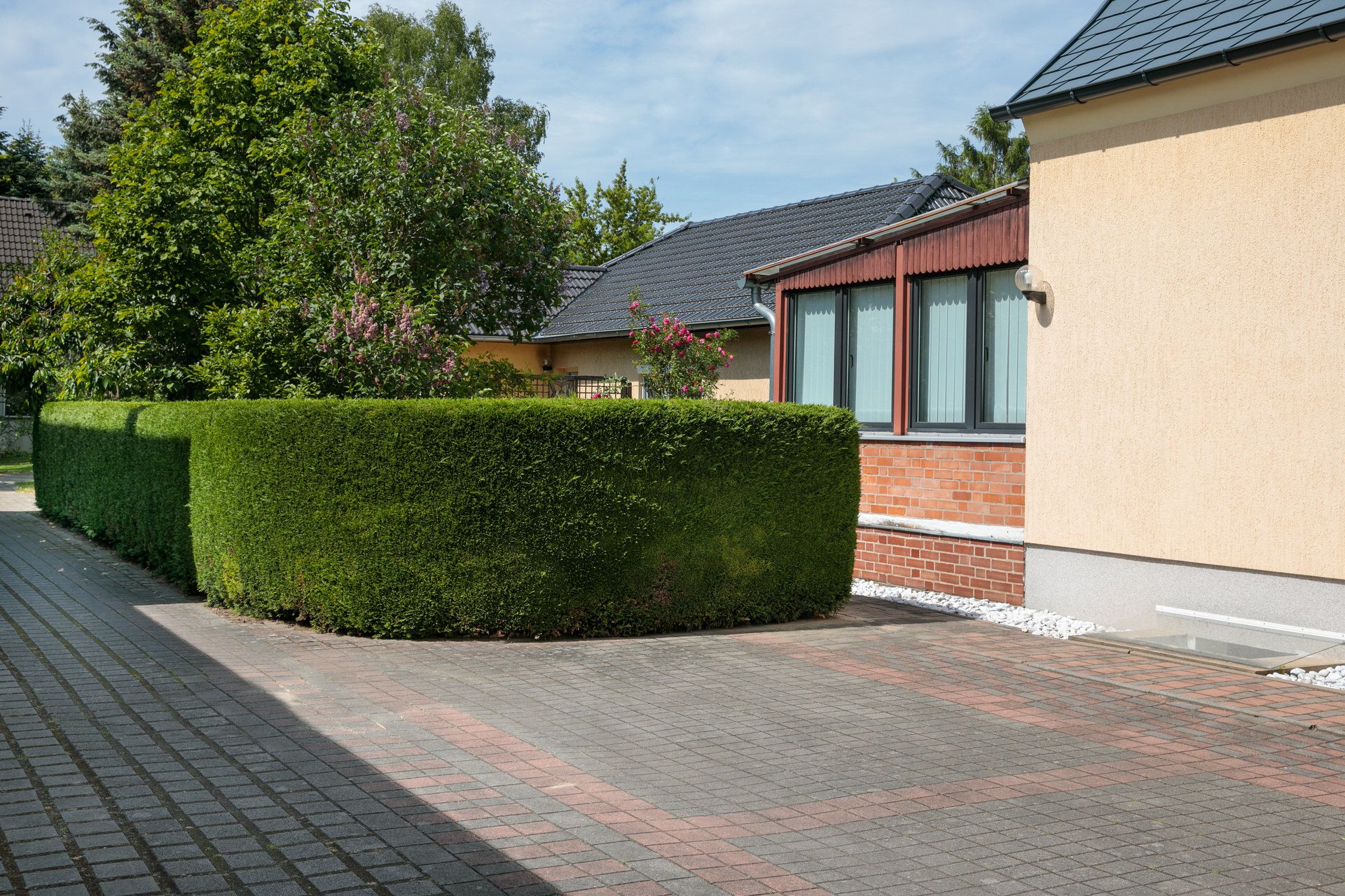 Gepflasterter Hof mit rechteckigen Hecken und einem Wohnhaus im Hintergrund.