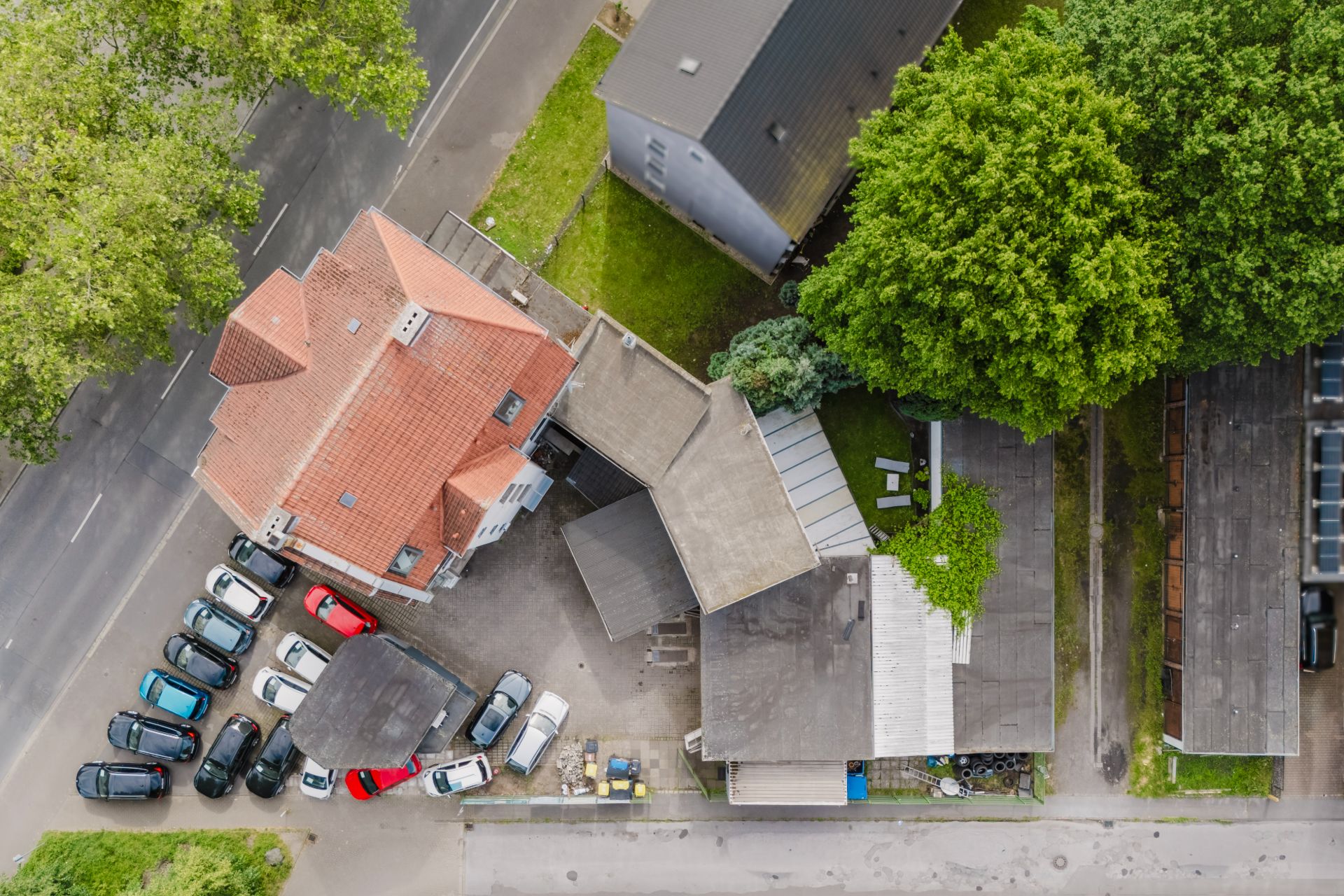 Luftaufnahme eines Hauses mit rotem Dach und angrenzendem Parkplatz mit mehreren Autos.