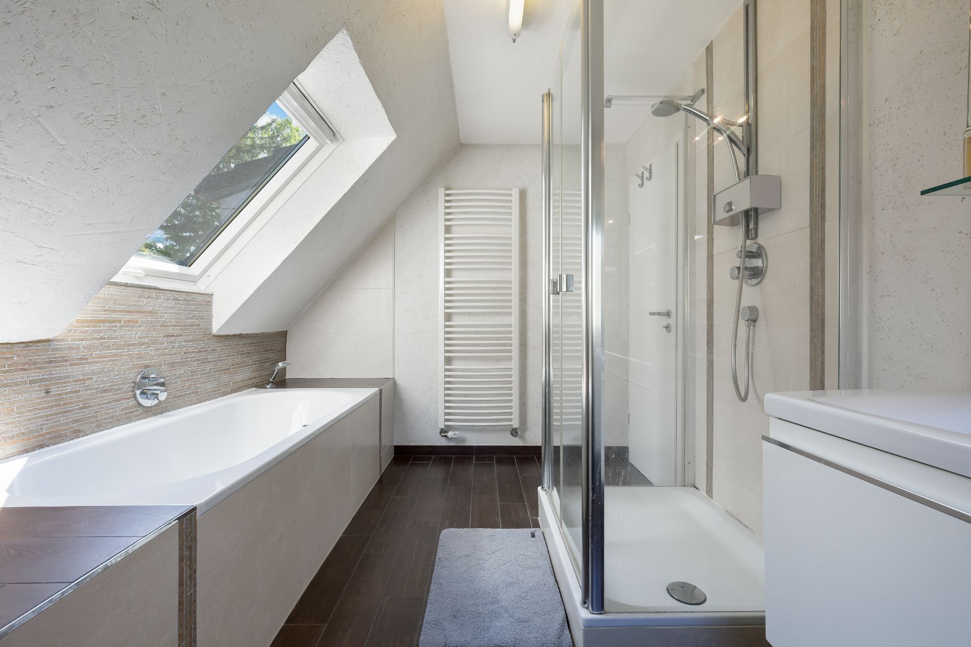 Modernes Bad mit Badewanne, Dusche, Waschbecken und Dachfenster.