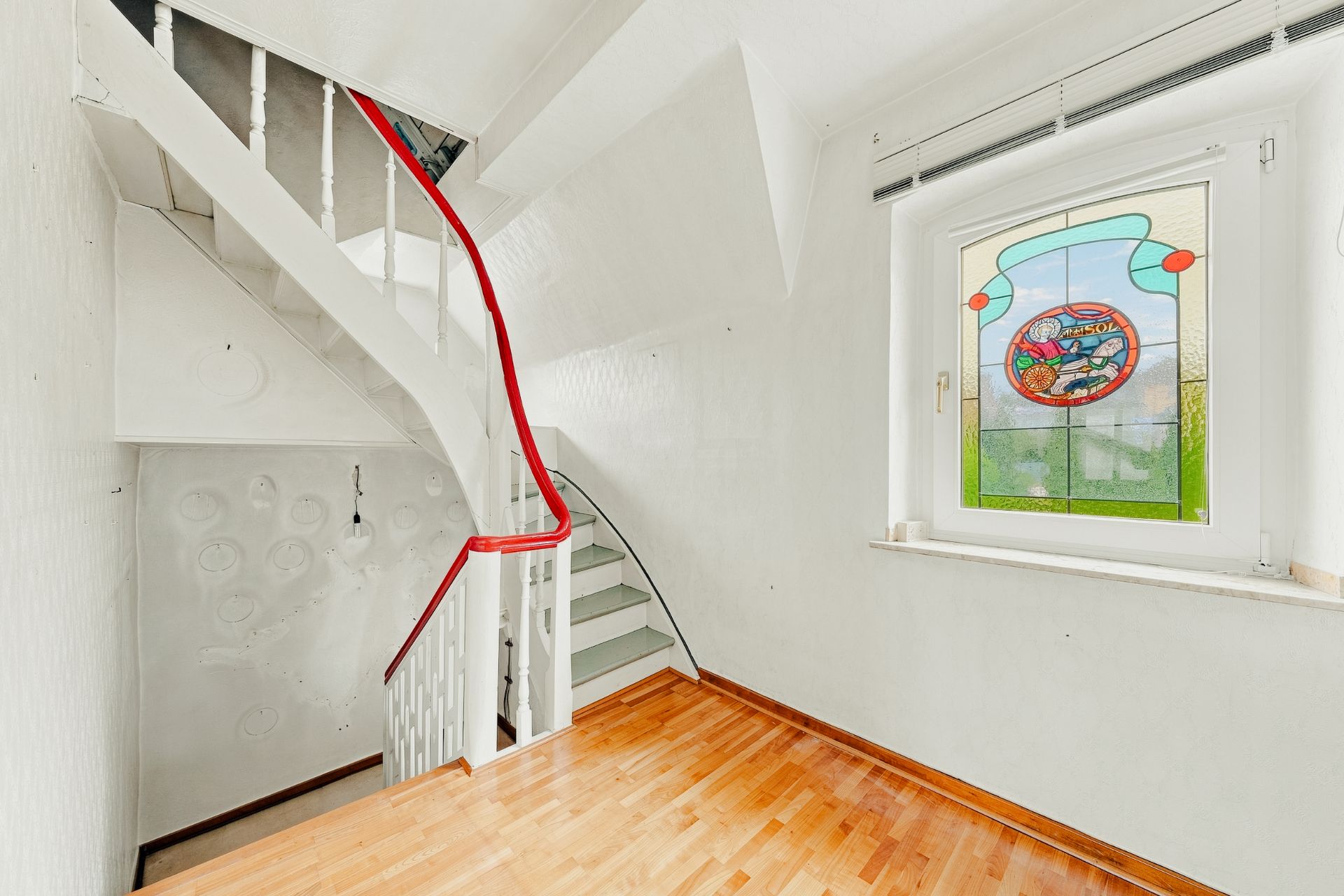 Heller Flur mit Holztreppe und Fenster mit buntem Glasbild.