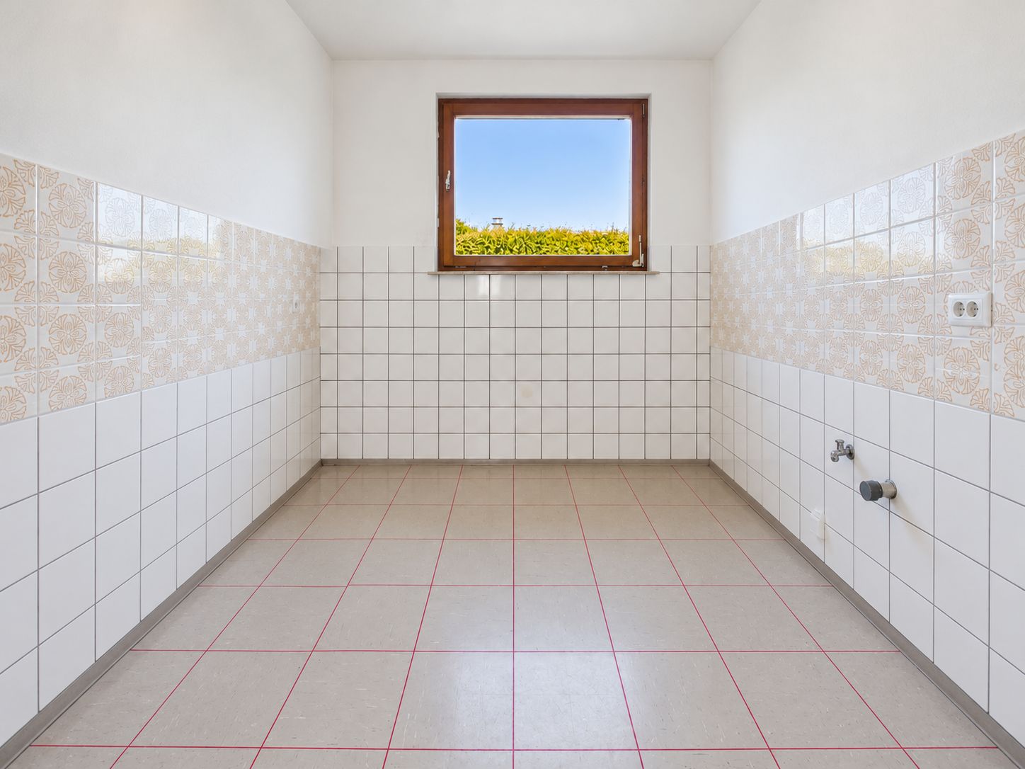 Leerer, gefliester Raum mit einem Fenster und Anschlüssen an der rechten Wand.