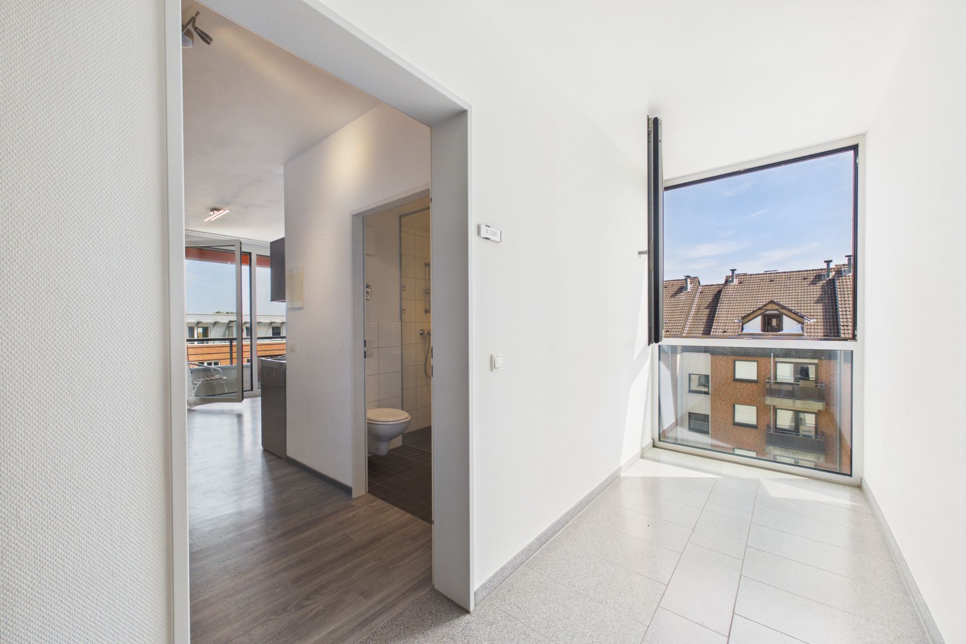 Heller Flur mit Blick in ein Bad und großes Fenster mit Aussicht auf Nachbarhäuser.