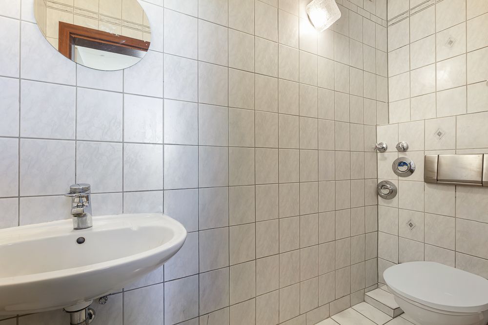 Gefliestes Badezimmer mit Waschbecken, Spiegel und wandhängender Toilette.