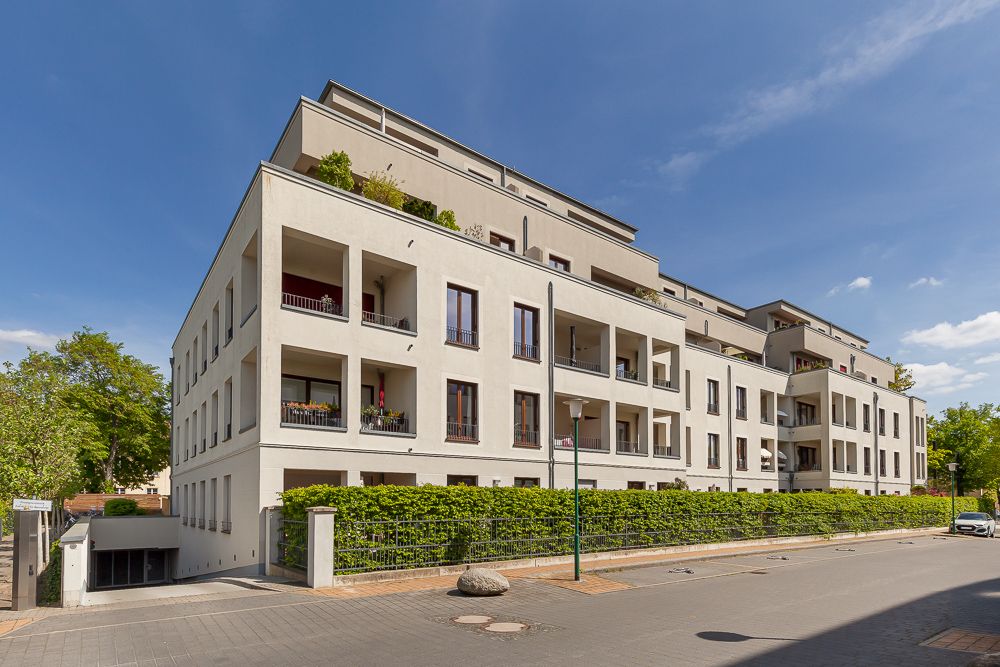 Modernes Wohngebäude mit mehreren Balkonen und umliegender Begrünung an einer ruhigen Straße.