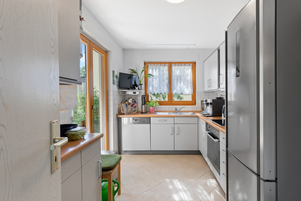 Helle Küche mit grauen Schränken, großem Fenster und Glastür zum Garten.