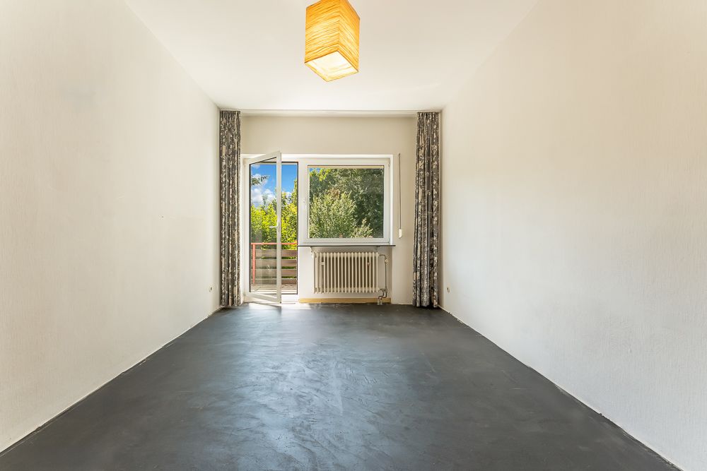 Leerer Raum mit dunklem Boden, Fenster, offener Tür zum Balkon und Vorhängen.