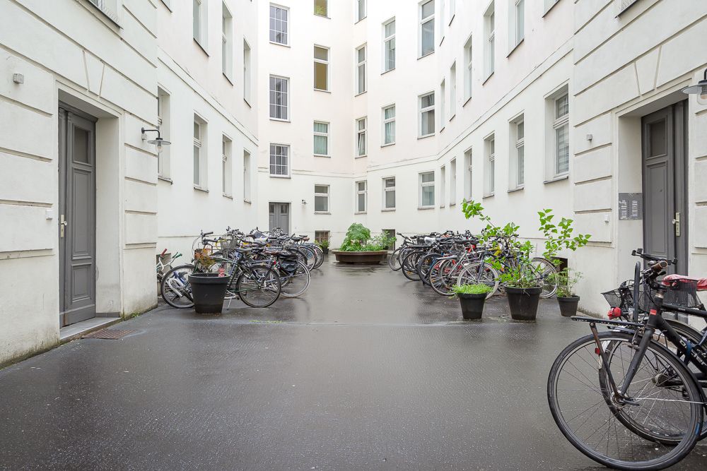 Innenhof eines Wohnhauses mit vielen abgestellten Fahrrädern und einigen Pflanzen in Töpfen.