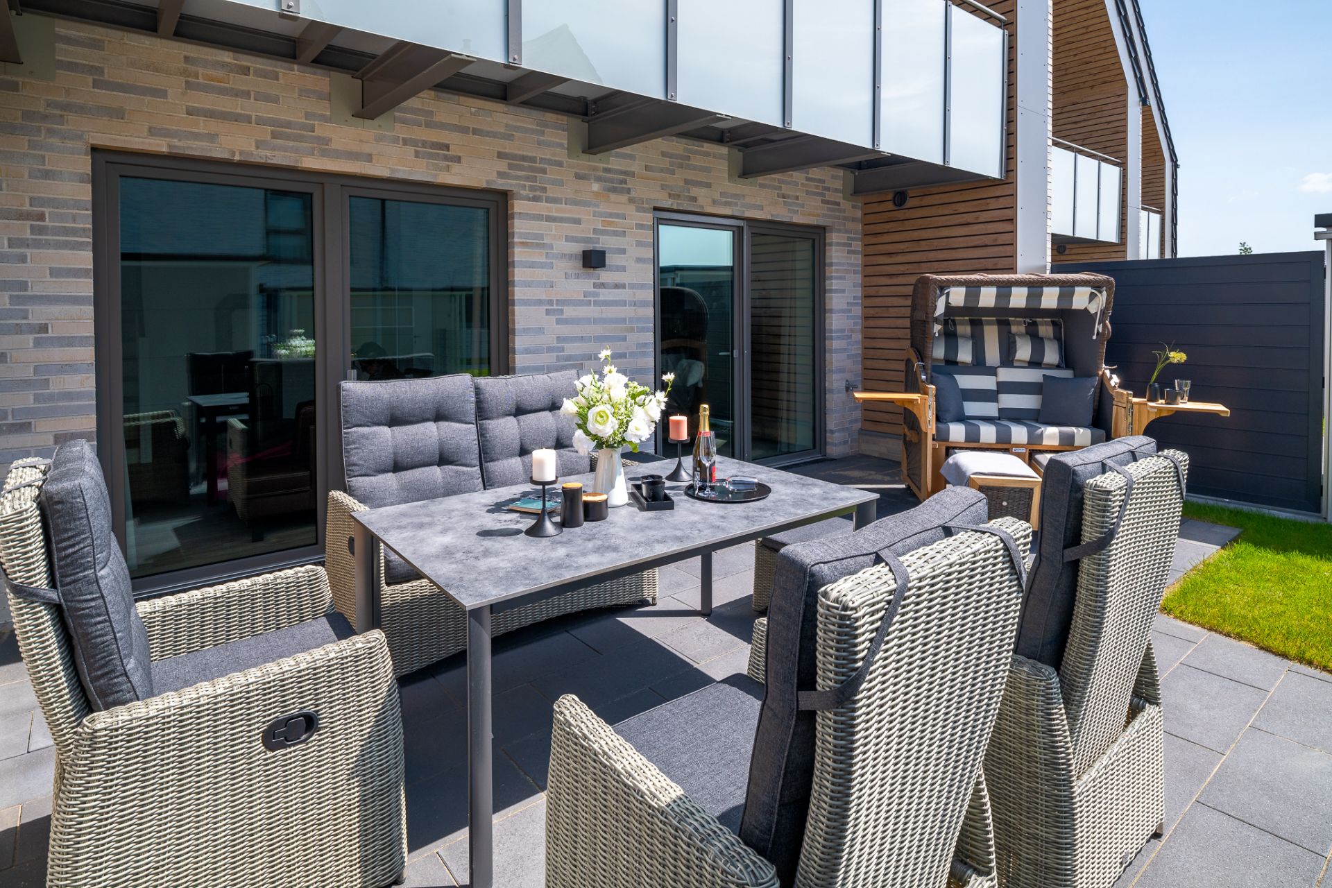 Moderne Terrasse mit Esstisch, sechs Stühlen und einem Strandkorb auf Steinfliesen.
