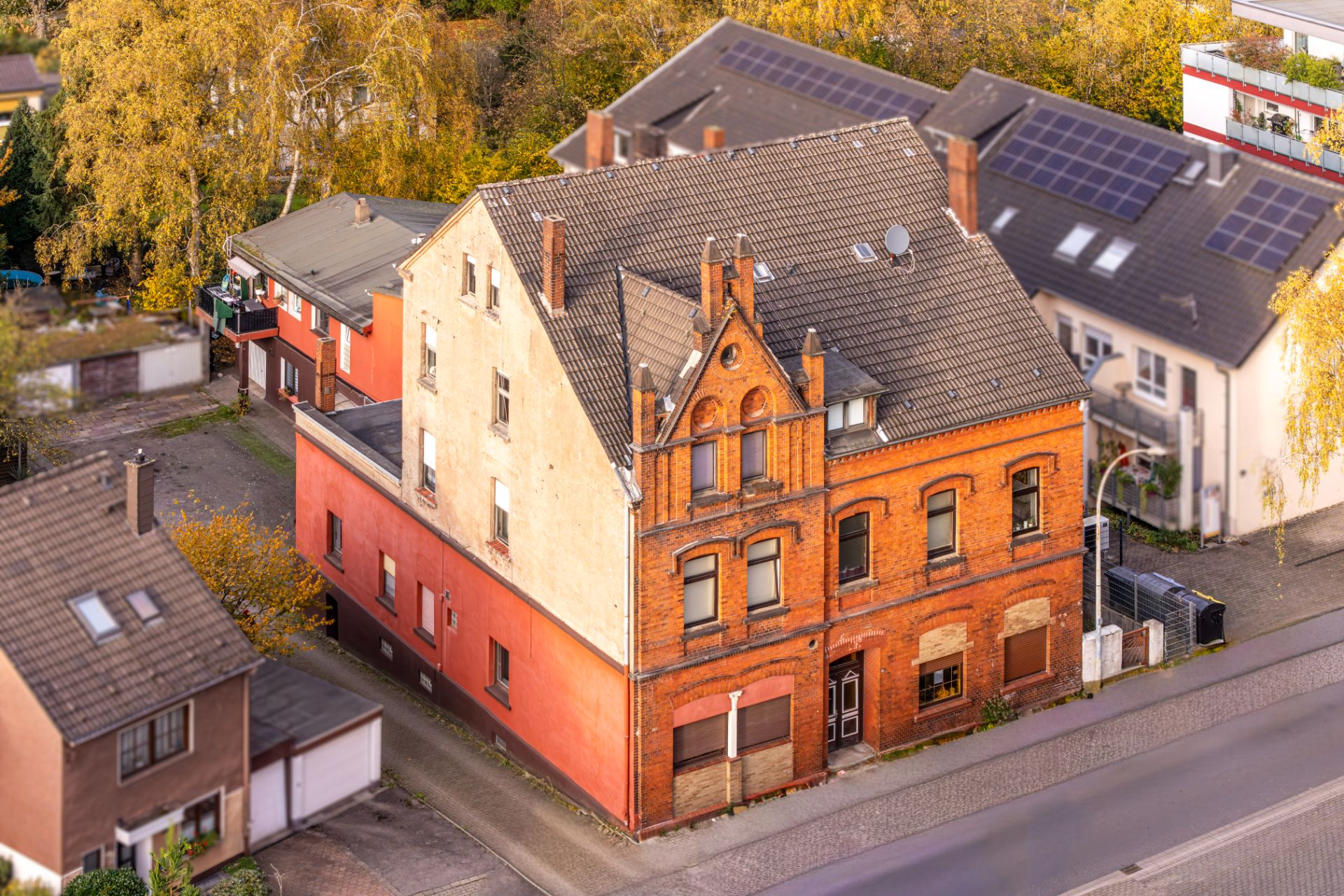 Altes Wohnhaus mit roter Backsteinfassade an einer Straße, umgeben von anderen Häusern.