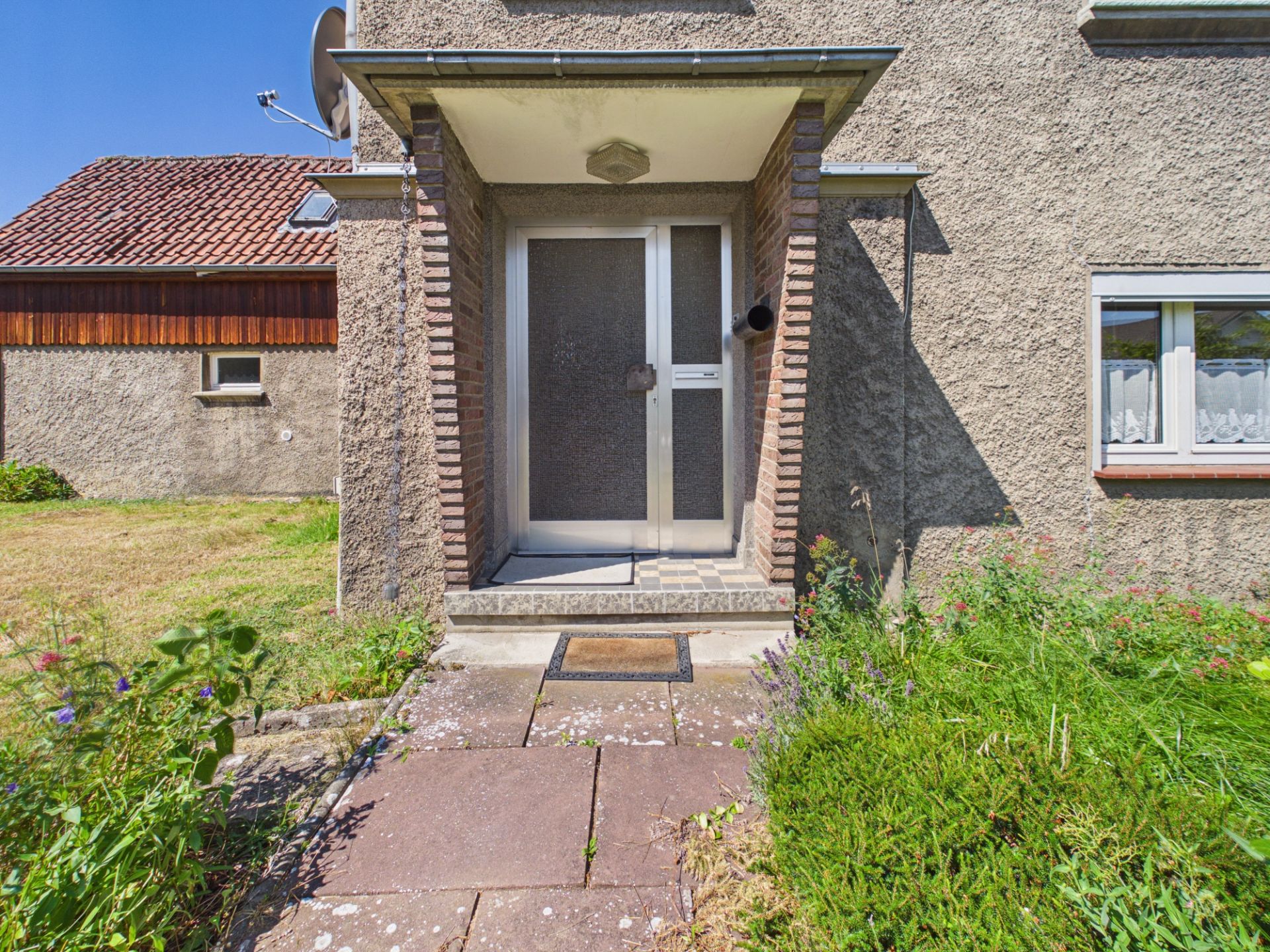 Eingangsbereich eines Wohnhauses mit Glastür, Vordach und Gartenweg.