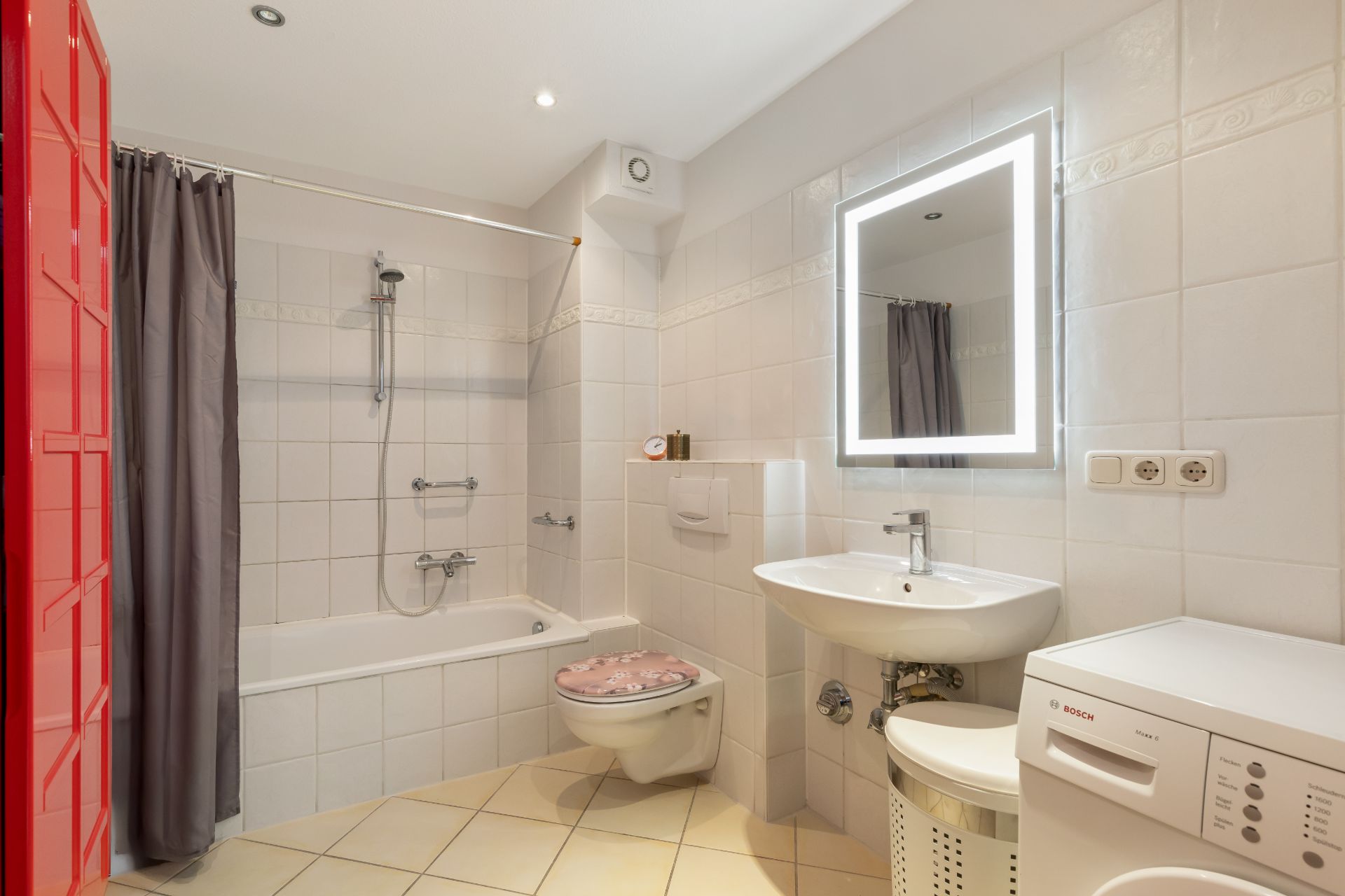 Modernes Badezimmer mit Badewanne, Waschbecken, beleuchtetem Spiegel, WC und Waschmaschine.