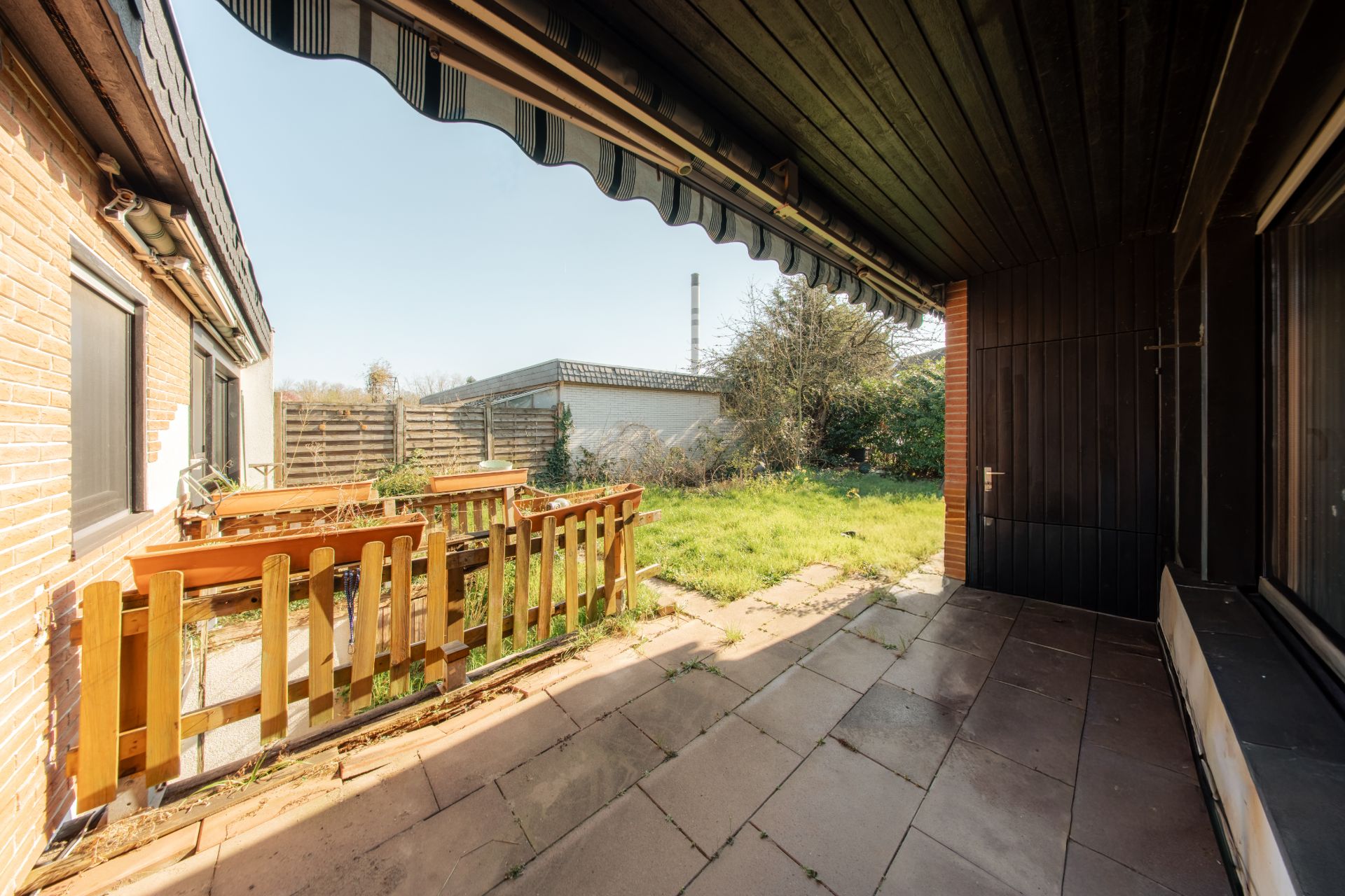 Überdachte Terrasse mit Holzzaun und Blick auf einen grasbewachsenen Garten.