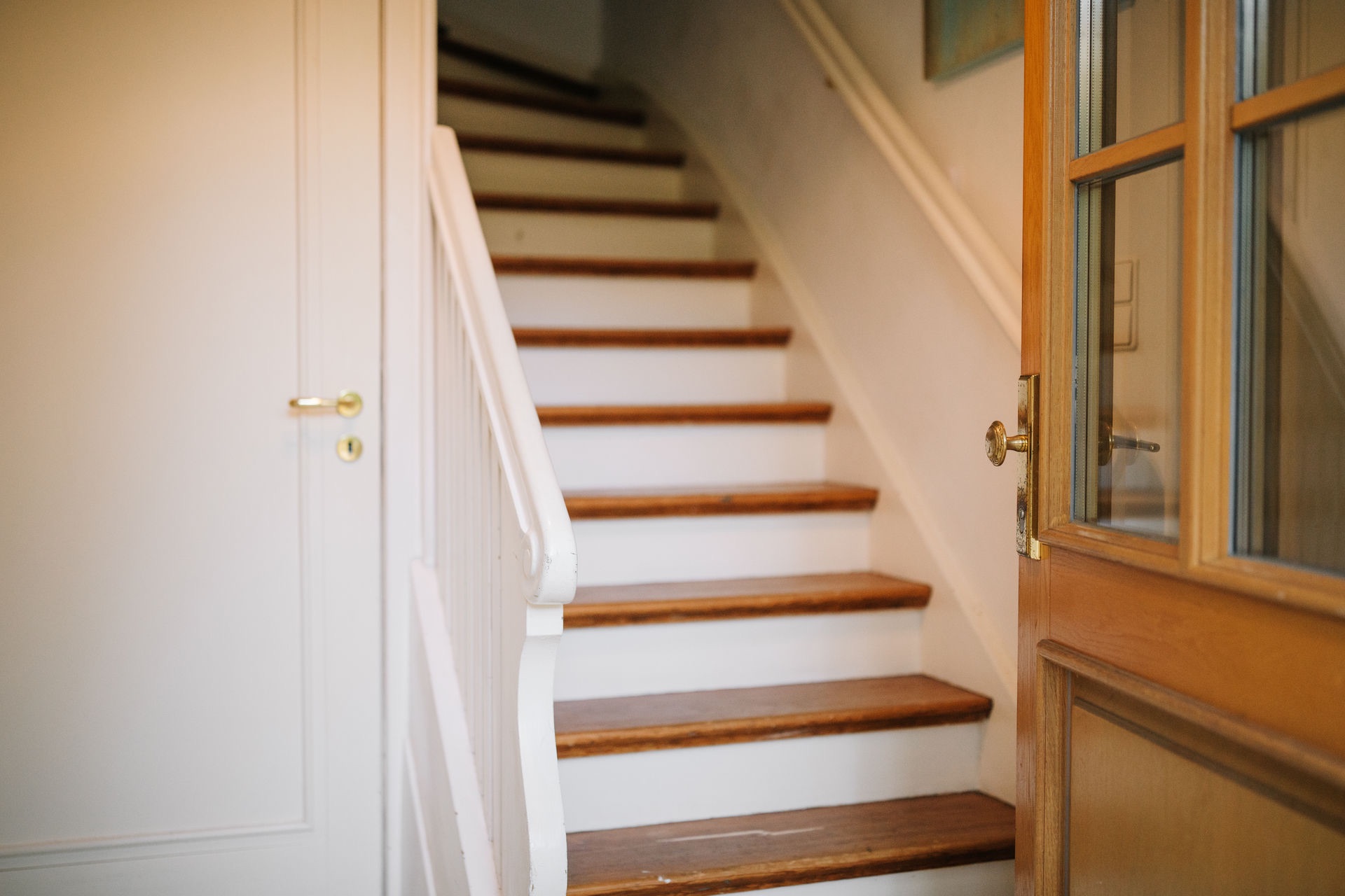 Eine hölzerne Treppe mit weißem Geländer in einem Eingangsbereich eines Hauses.