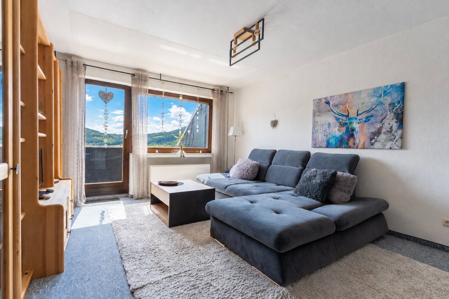 Wohnzimmer mit grauem Sofa, Couchtisch, Teppich und großem Fenster mit Bergblick.