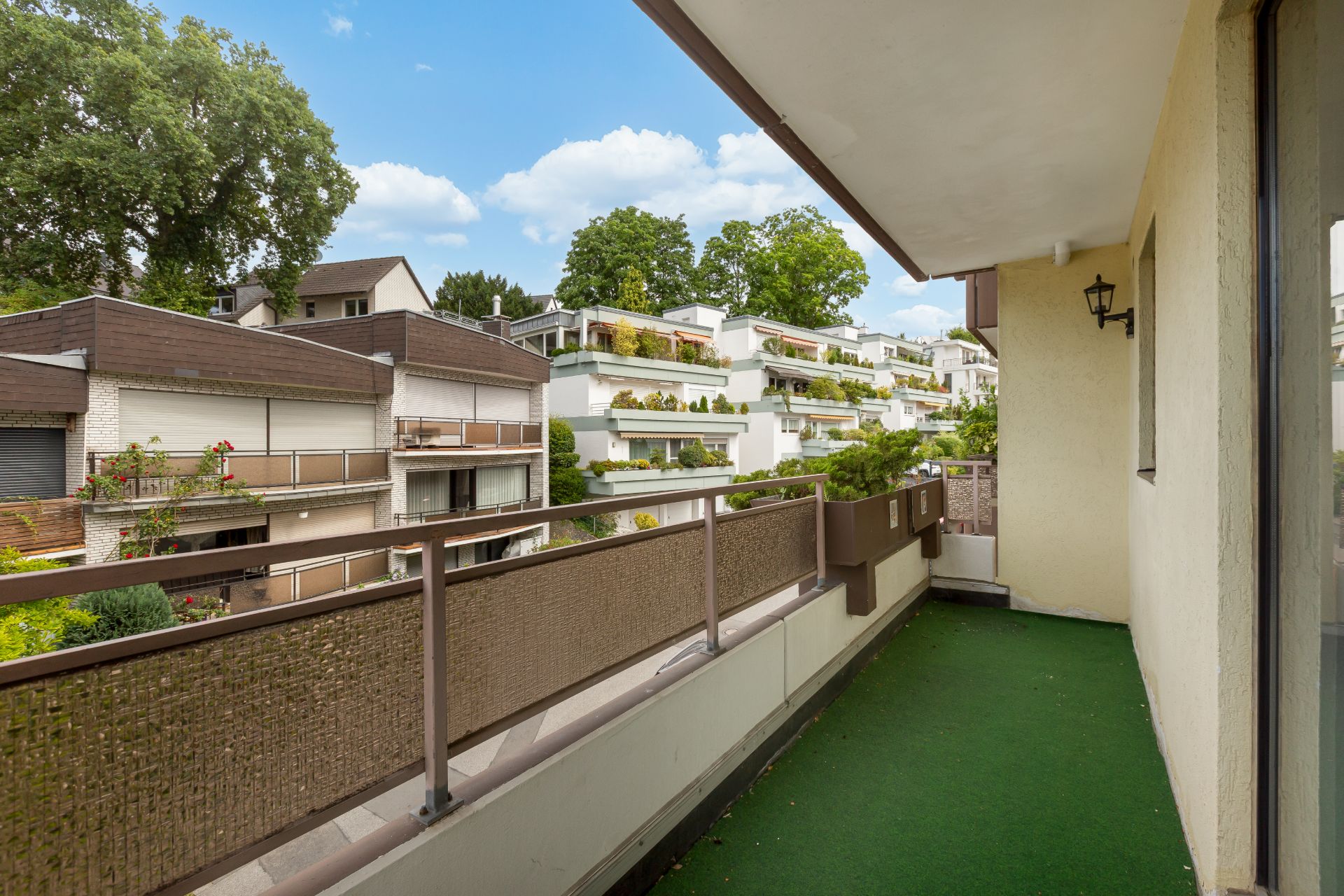 Balkon mit grünem Bodenbelag und Blick auf benachbarte Wohngebäude und Bäume.
