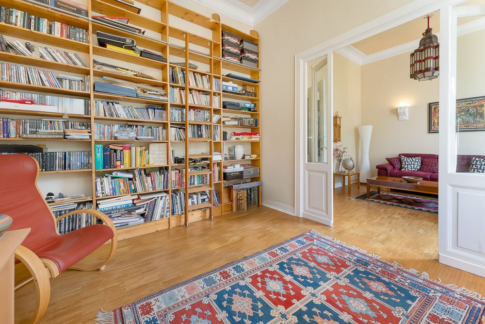 Wohnzimmer mit Bücherregal, rotem Sessel und Blick in ein zweites Zimmer mit Sofa und Couchtisch.