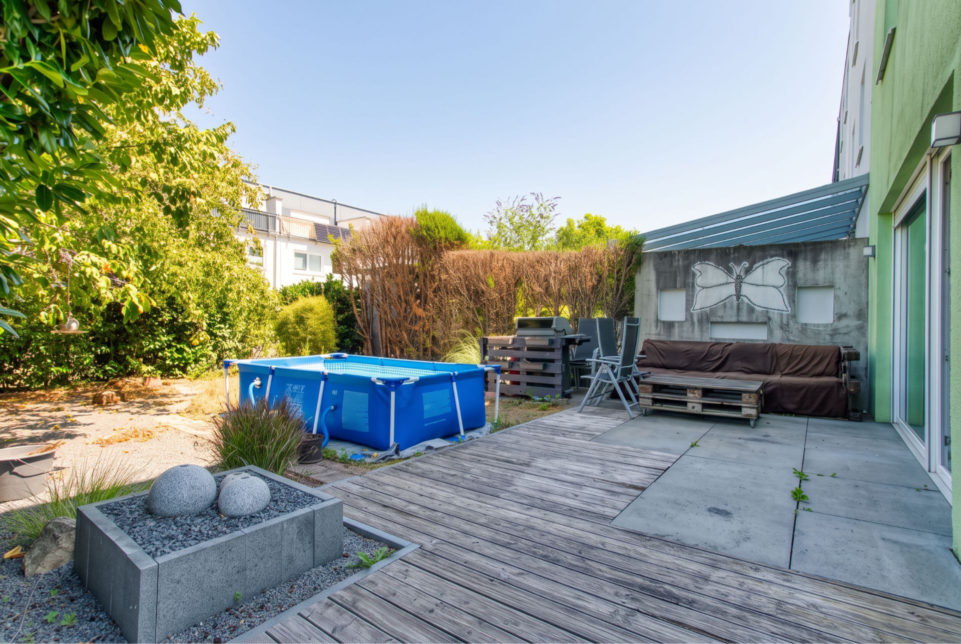 Garten mit Holzterrasse, kleinem Pool, Palettensofa und moderner Bepflanzung.