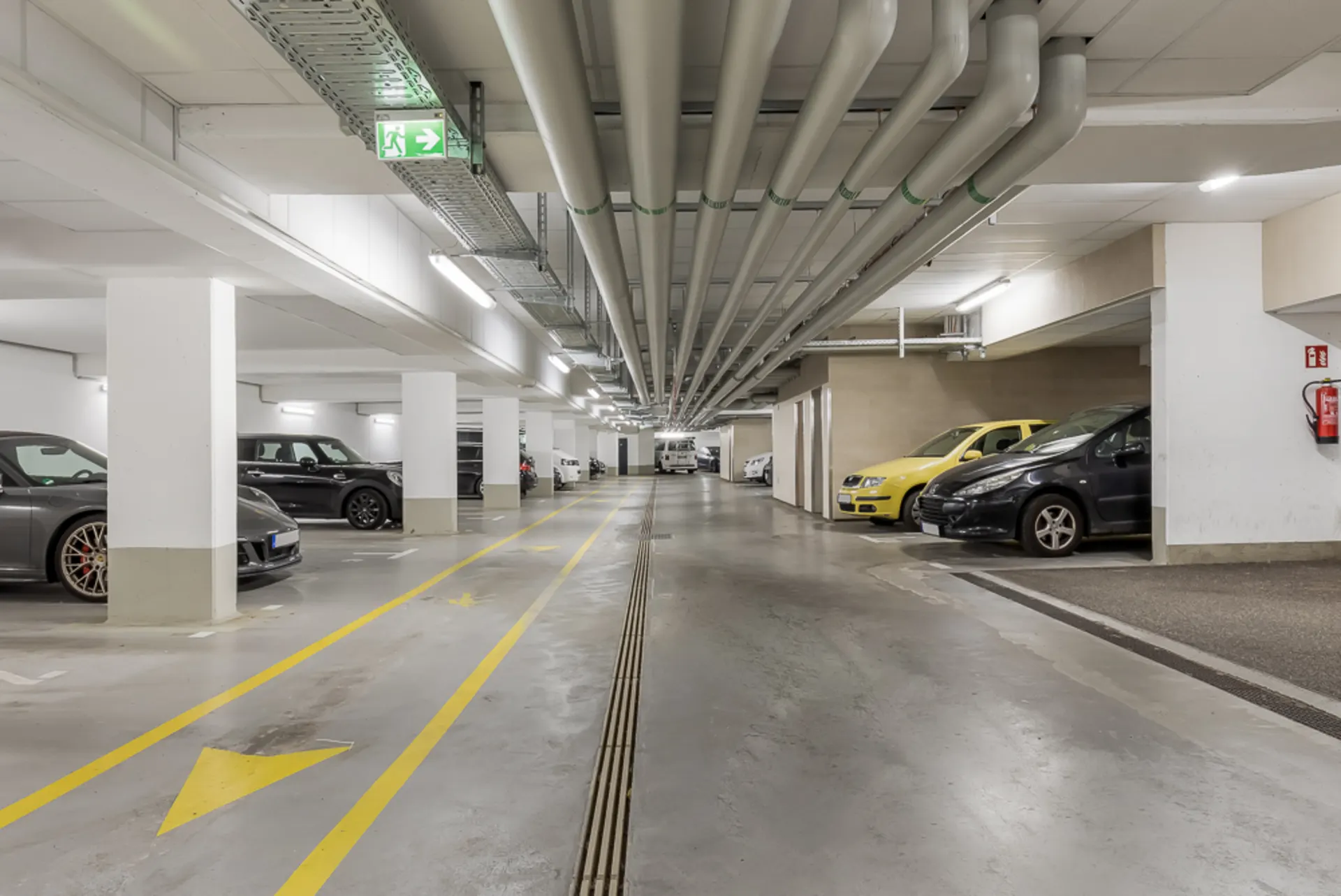 Helle Tiefgarage mit mehreren geparkten Autos und gelben Markierungen auf dem Boden.