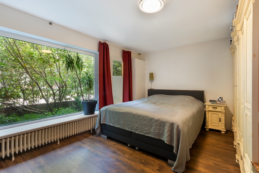 Schlafzimmer mit großem Fenster, Doppelbett, Nachttisch und Holzboden.