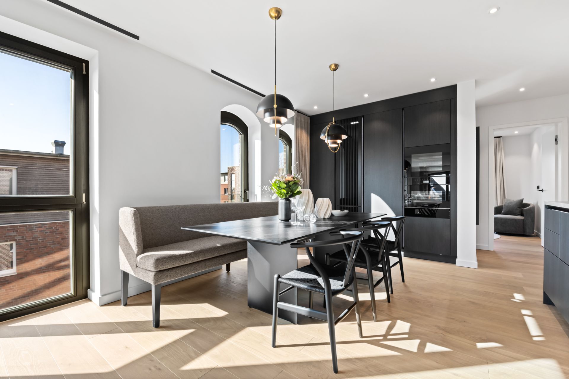 Helles Esszimmer mit schwarzem Tisch, Eckbank, Stühlen und zwei modernen Hängeleuchten.