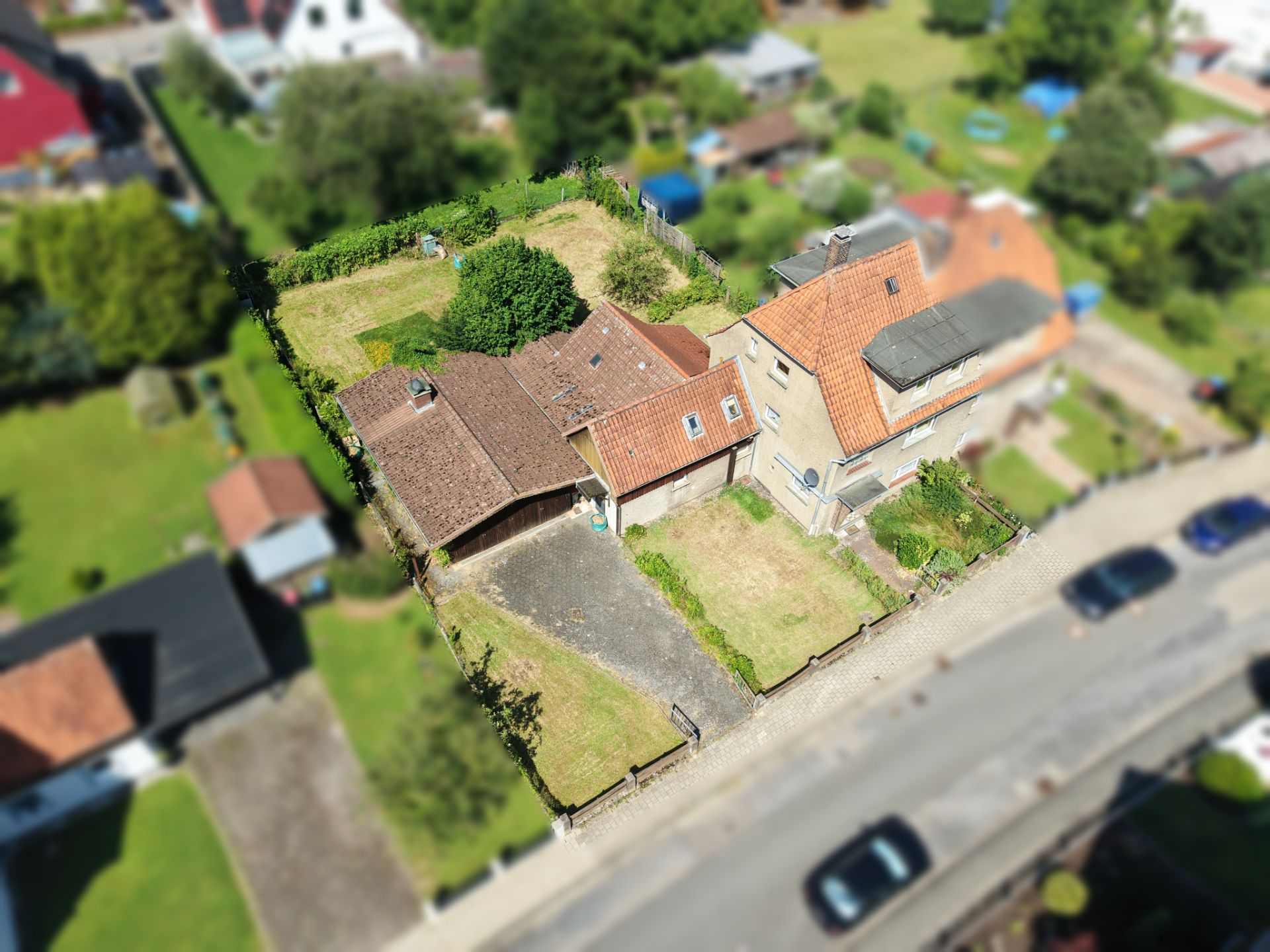 Luftaufnahme eines Hauses mit Garage, Garten und Einfahrt an einer Straße.