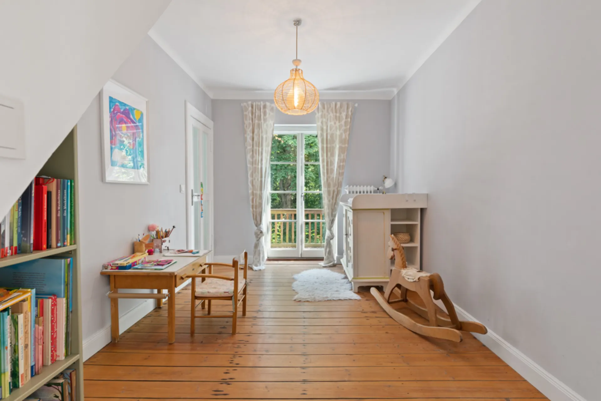 Helles Kinderzimmer mit Schreibtisch, Bücherregal, Wickelkommode und Schaukelpferd.