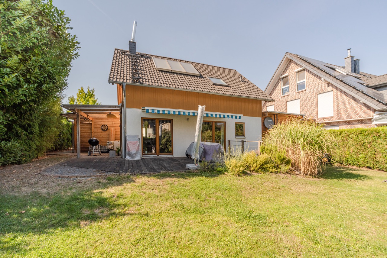 Modernes Einfamilienhaus mit Terrasse, Markise und Garten bei sonnigem Wetter.
