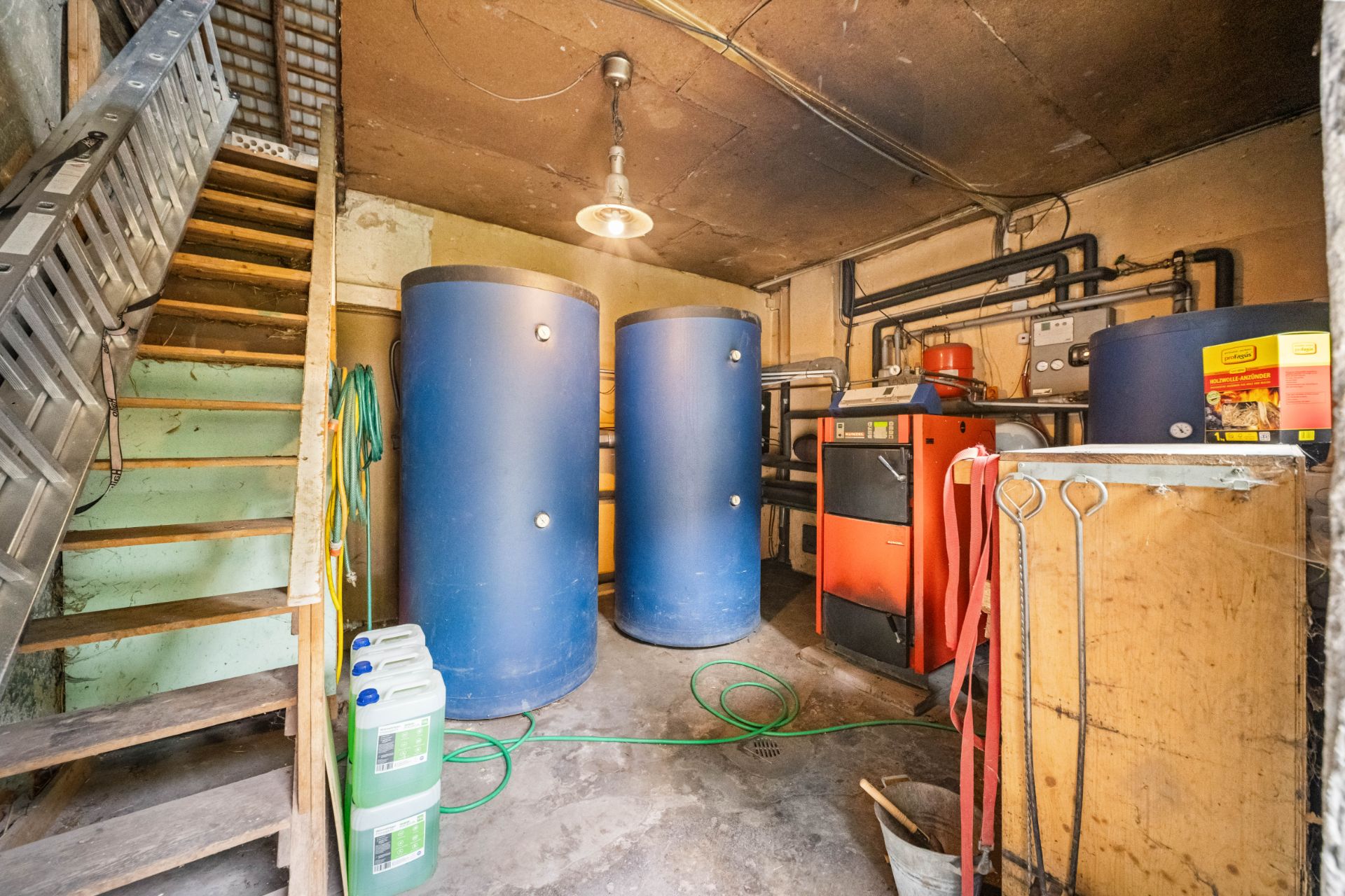 Hauswirtschaftsraum mit zwei blauen Tanks, Heizanlage, Treppe und Kanistern.