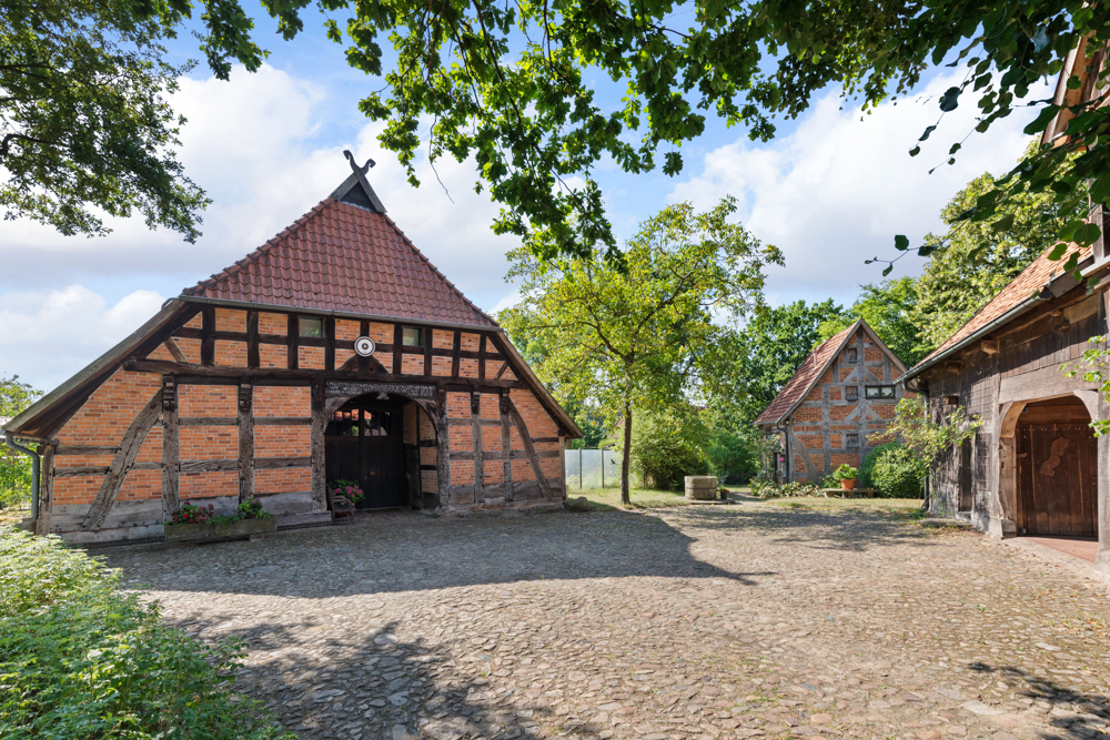 Gepflasterter Hof mit mehreren Fachwerkhäusern und Bäumen an einem sonnigen Tag.