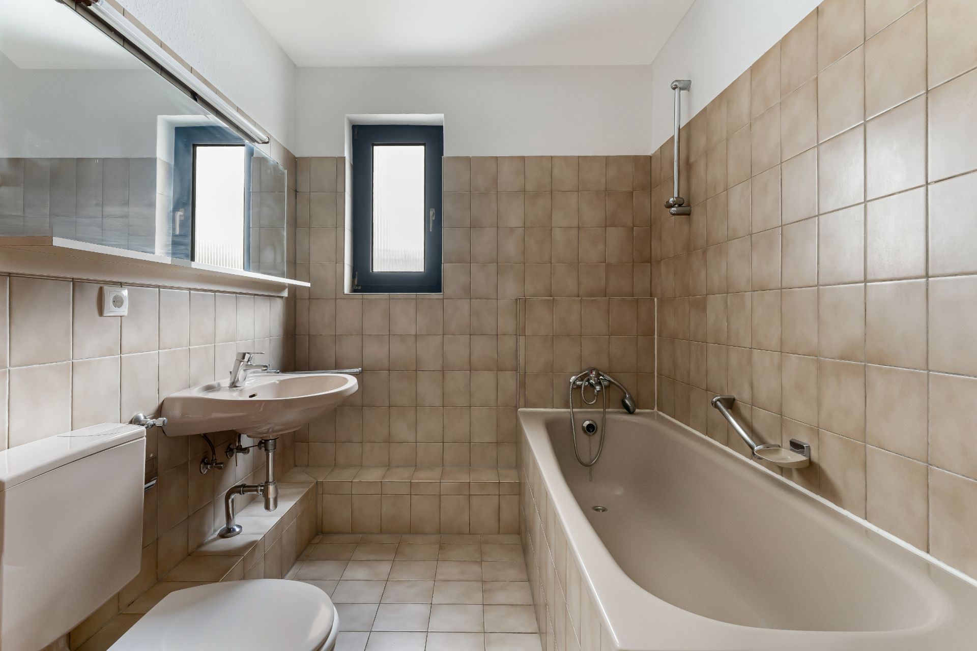 Helles Badezimmer mit Badewanne, Waschbecken, Toilette und kleinem Fenster.