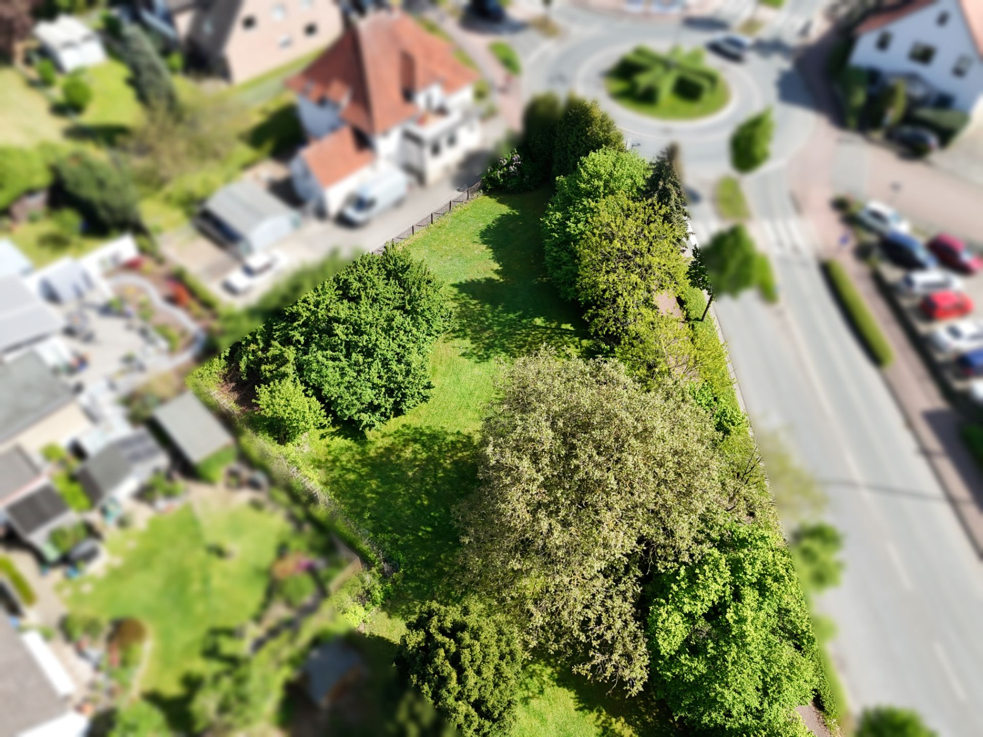 Luftaufnahme eines grünen Gartengrundstücks mit Bäumen und Büschen an einer Straßenkreuzung.
