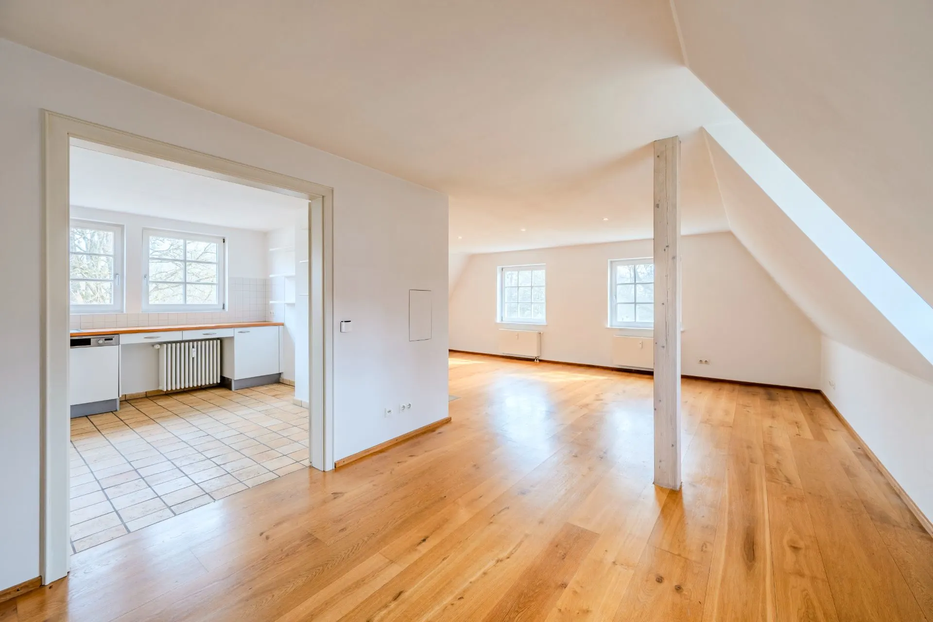 Helles Wohnzimmer mit Holzfußboden und angrenzender Küche in einer Dachgeschosswohnung.