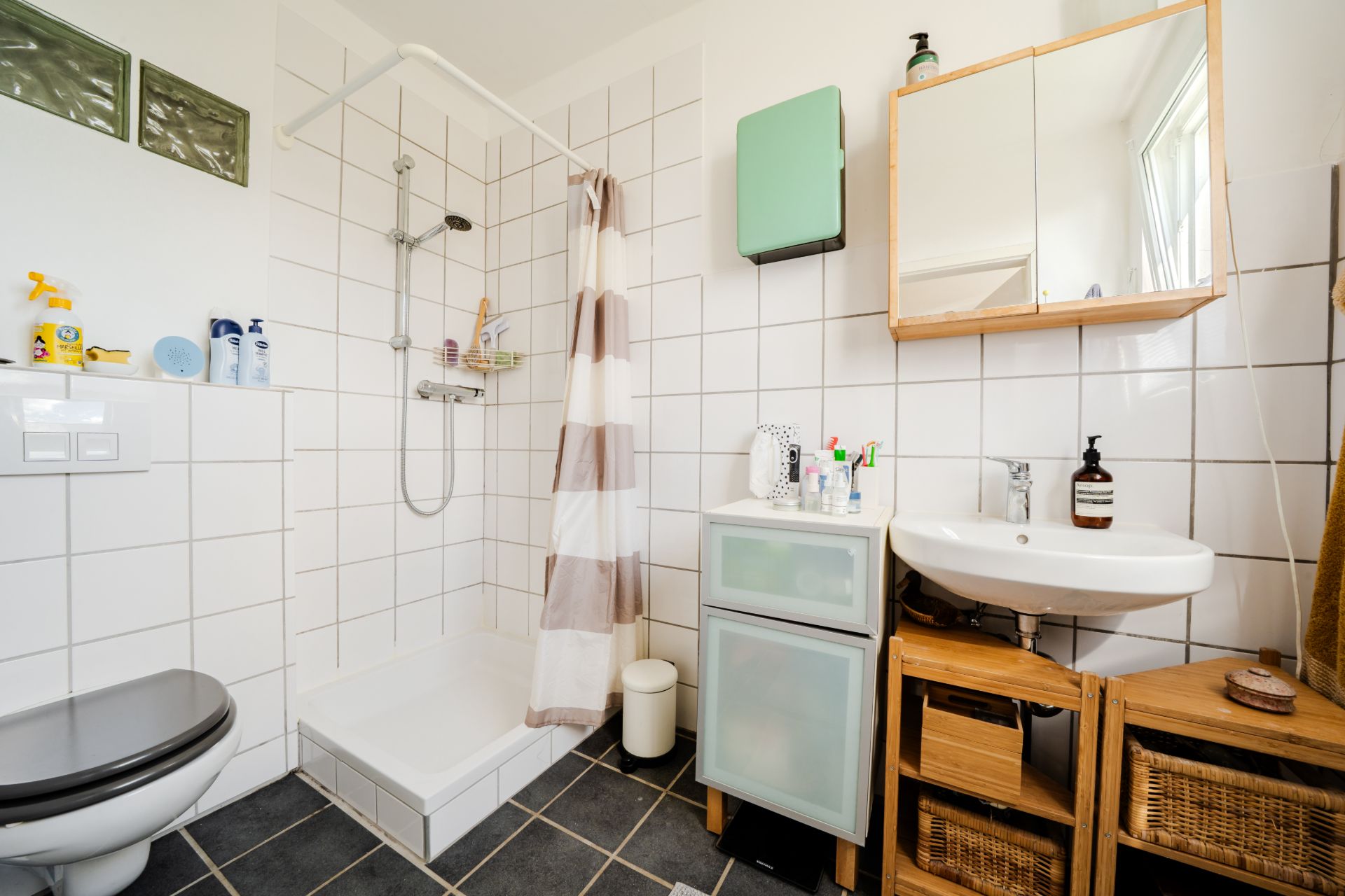 Modernes Badezimmer mit Dusche, WC, Spiegel, Waschbecken und weißen Fliesen.