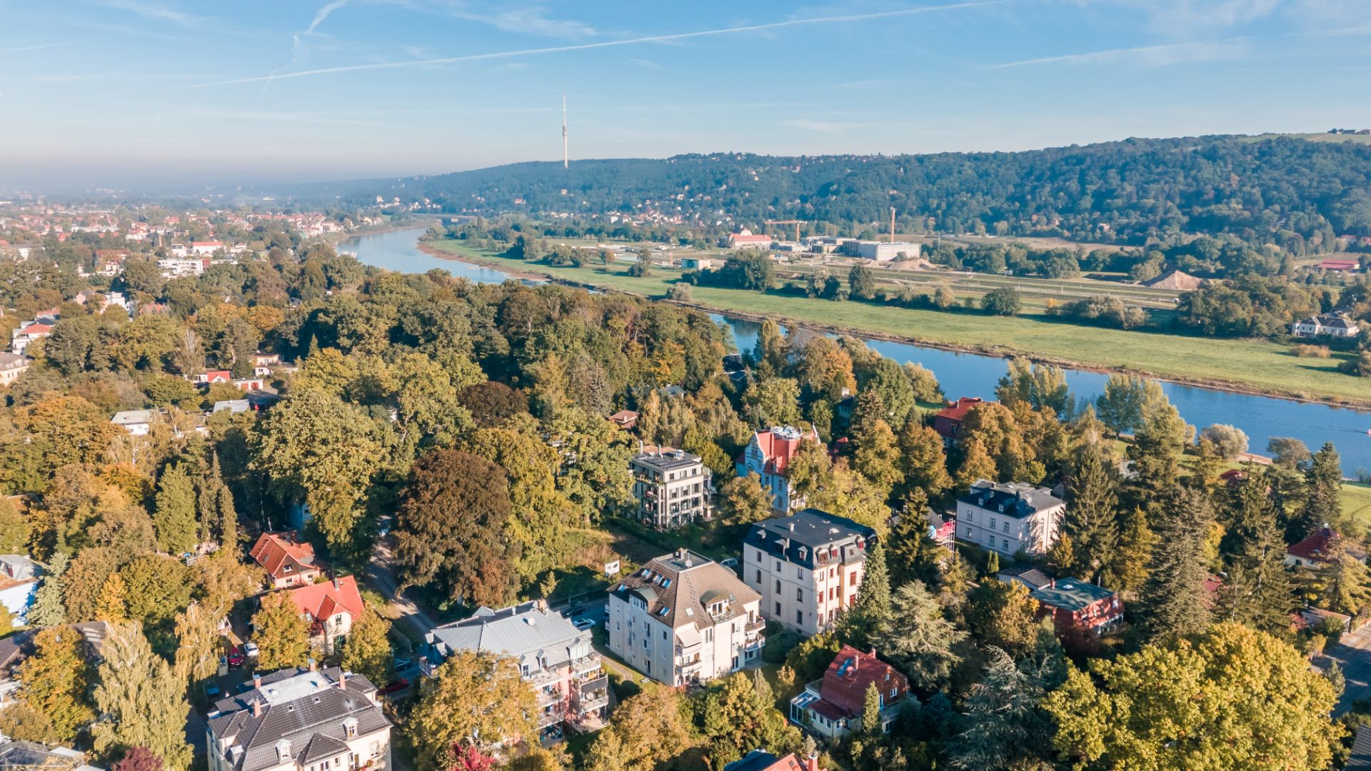 Luftaufnahme von Wohnhäusern mit viel Grün und einem Fluss im Hintergrund.