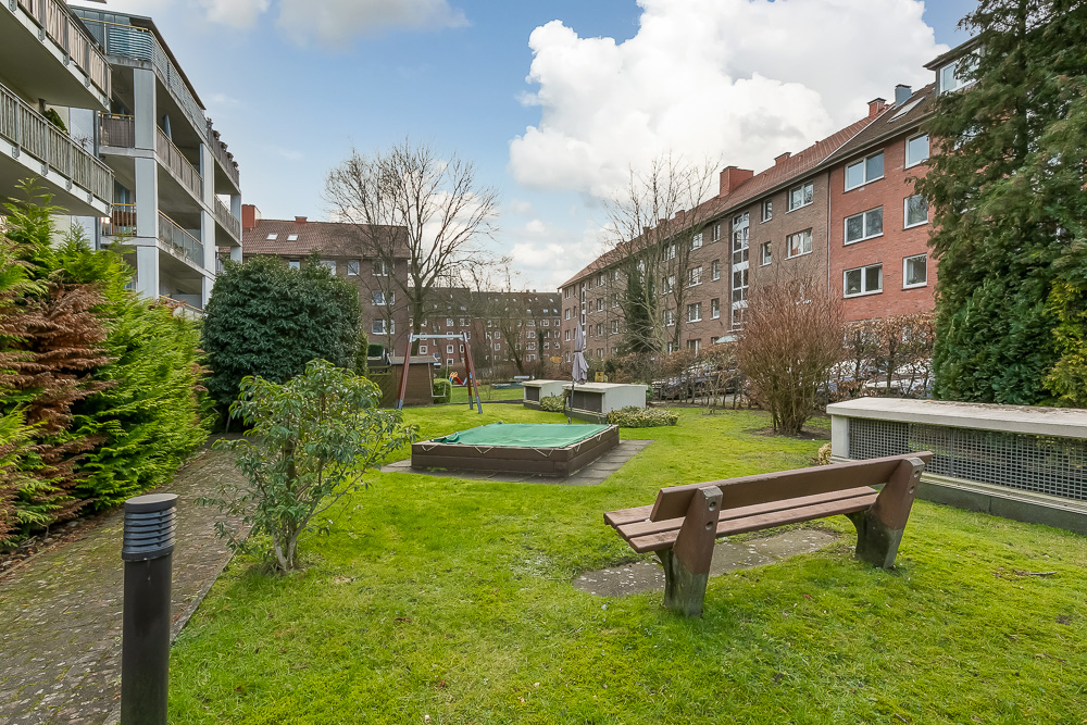 Grüner Innenhof mit Bank, Sandkasten und umgebenden Wohngebäuden.