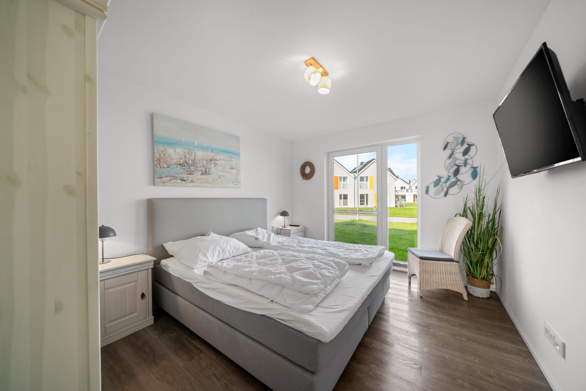 Helles Schlafzimmer mit Doppelbett, großem Fenster, Fernseher und Pflanzen.