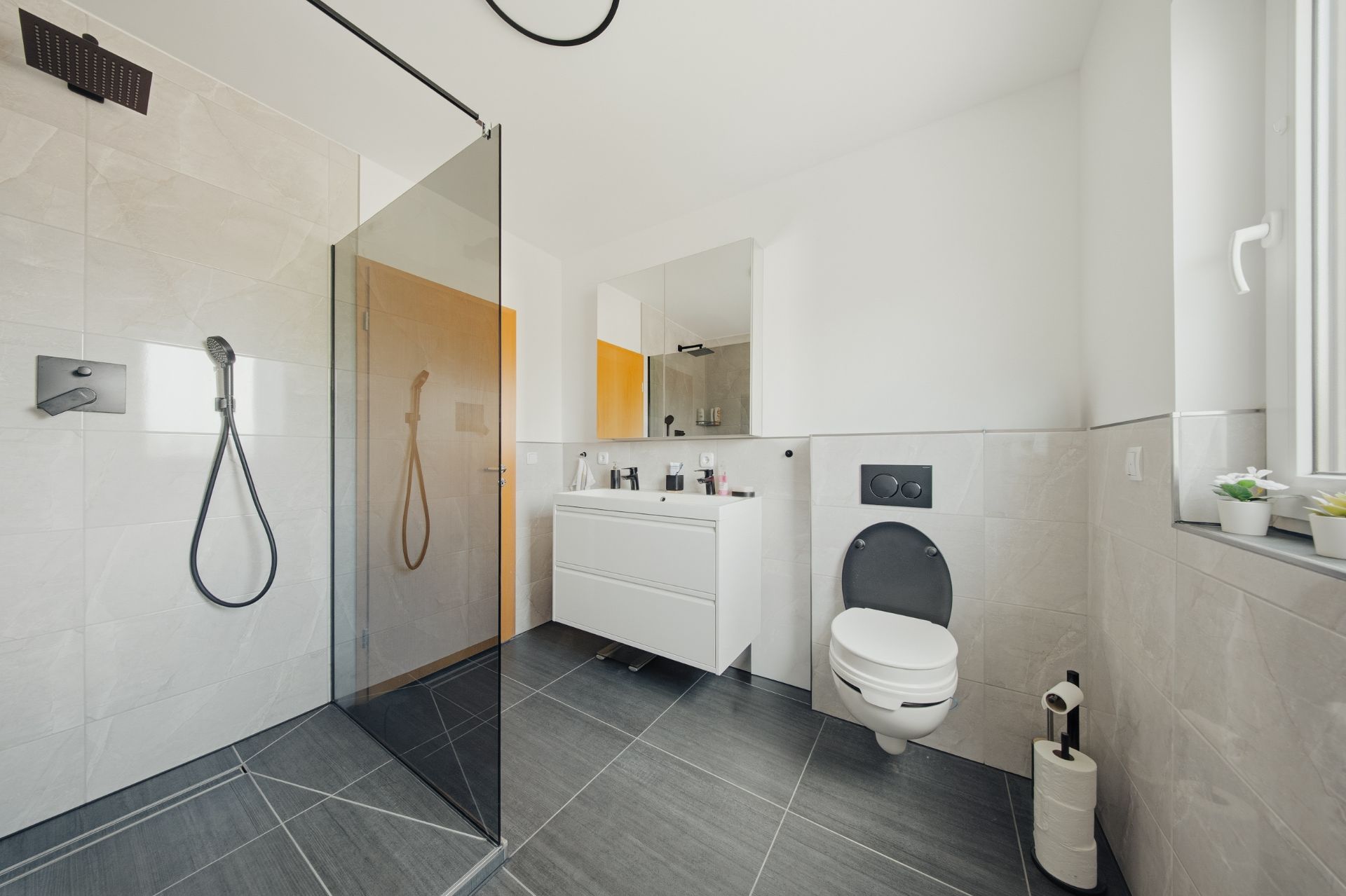 Modernes Badezimmer mit ebenerdiger Dusche, WC, Waschbecken und großem Spiegel.