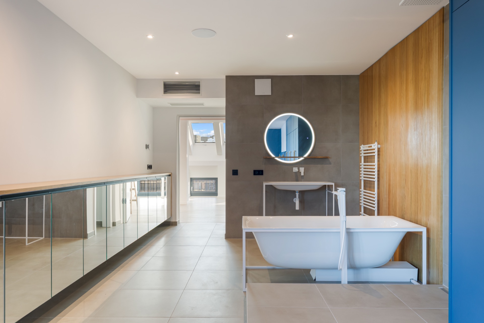 Modernes Badezimmer mit freistehender Badewanne, rundem Spiegel und Holzwand.